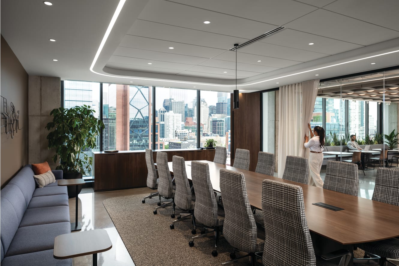 Conference seating area with upholstered rolling chairs, lounge sofa with cushioned seating, and compact side tables with wood tops and slim bases.