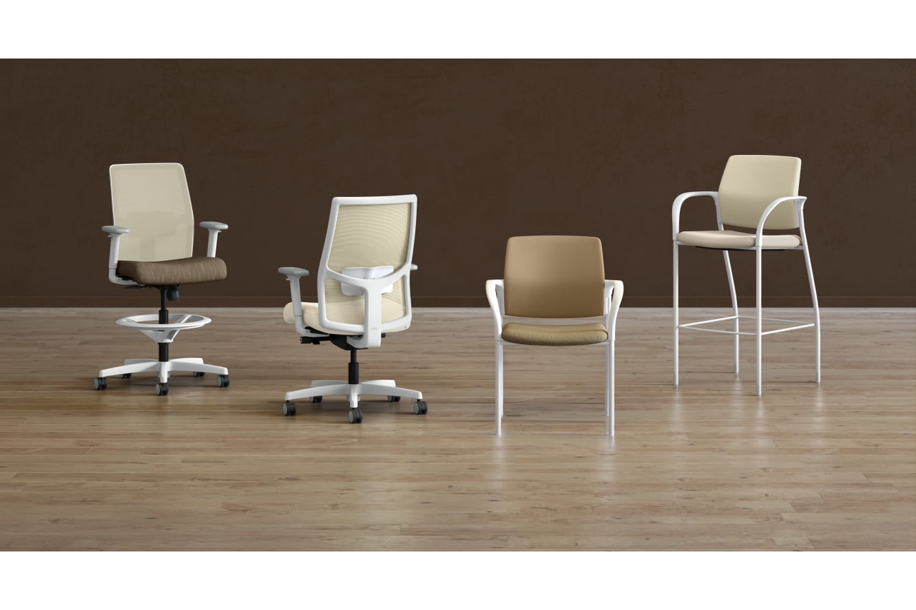 A collection of modern office chairs in various styles and colors, arranged on a wooden floor against a plain brown background.