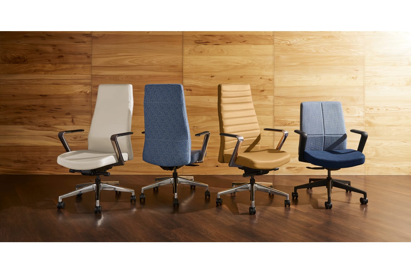 The image shows several office chairs of different designs and colors arranged in front of a wooden wall.