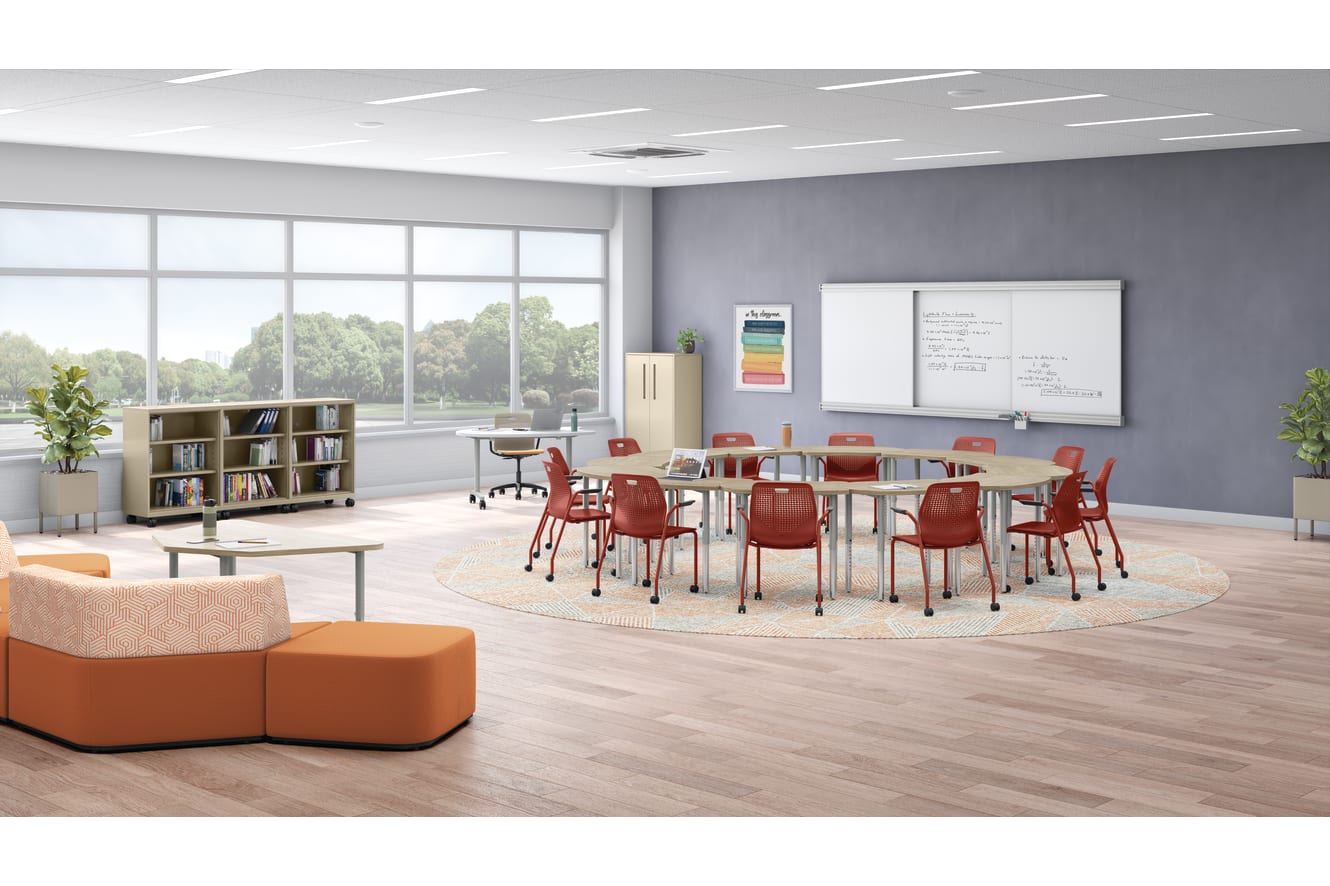 A modern, well-lit classroom with a large table surrounded by red chairs, bookshelves, and a whiteboard on the wall. The room has large windows overlooking a scenic outdoor area.