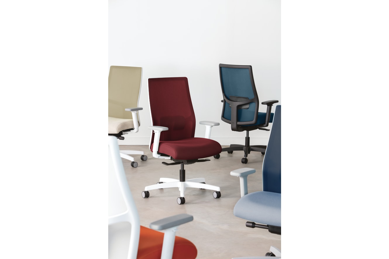The image depicts a collection of modern office chairs in various colors, including beige, brown, and purple, arranged on a light-colored floor.