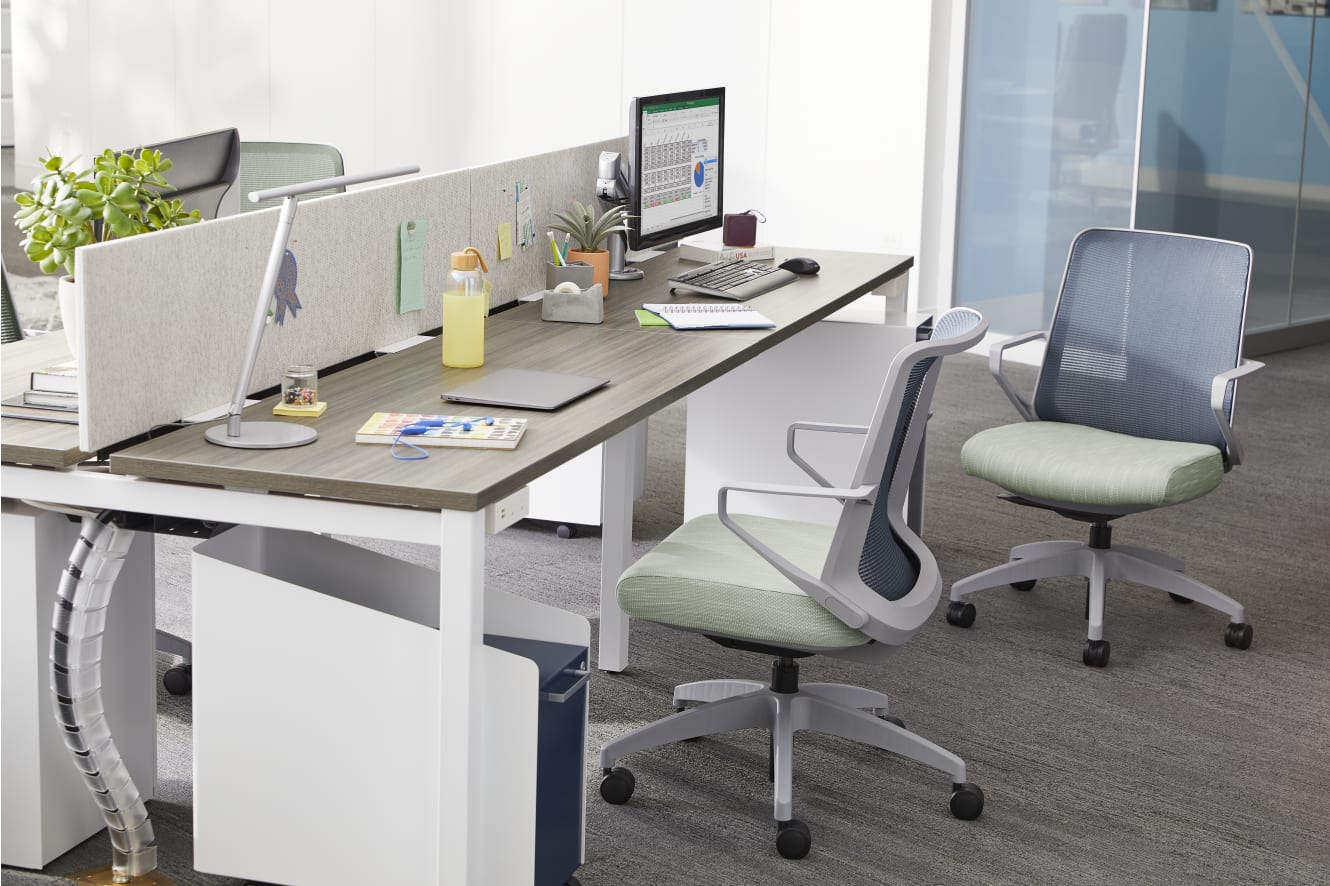 A modern, minimalist office workspace with a desk, computer, and various office supplies and accessories, set against a plain white wall background.