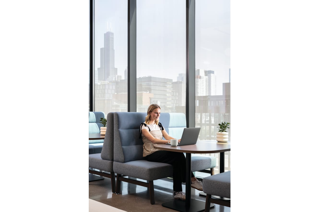 Round pedestal table with wood top and black base, paired with soft seating for casual work or conversation.