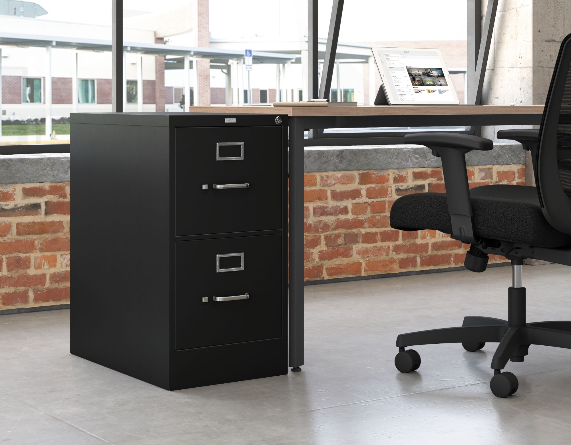 A black filing cabinet stands in the foreground, with a desk and office chair visible in the background. The room features exposed brick walls, creating a modern and industrial aesthetic.