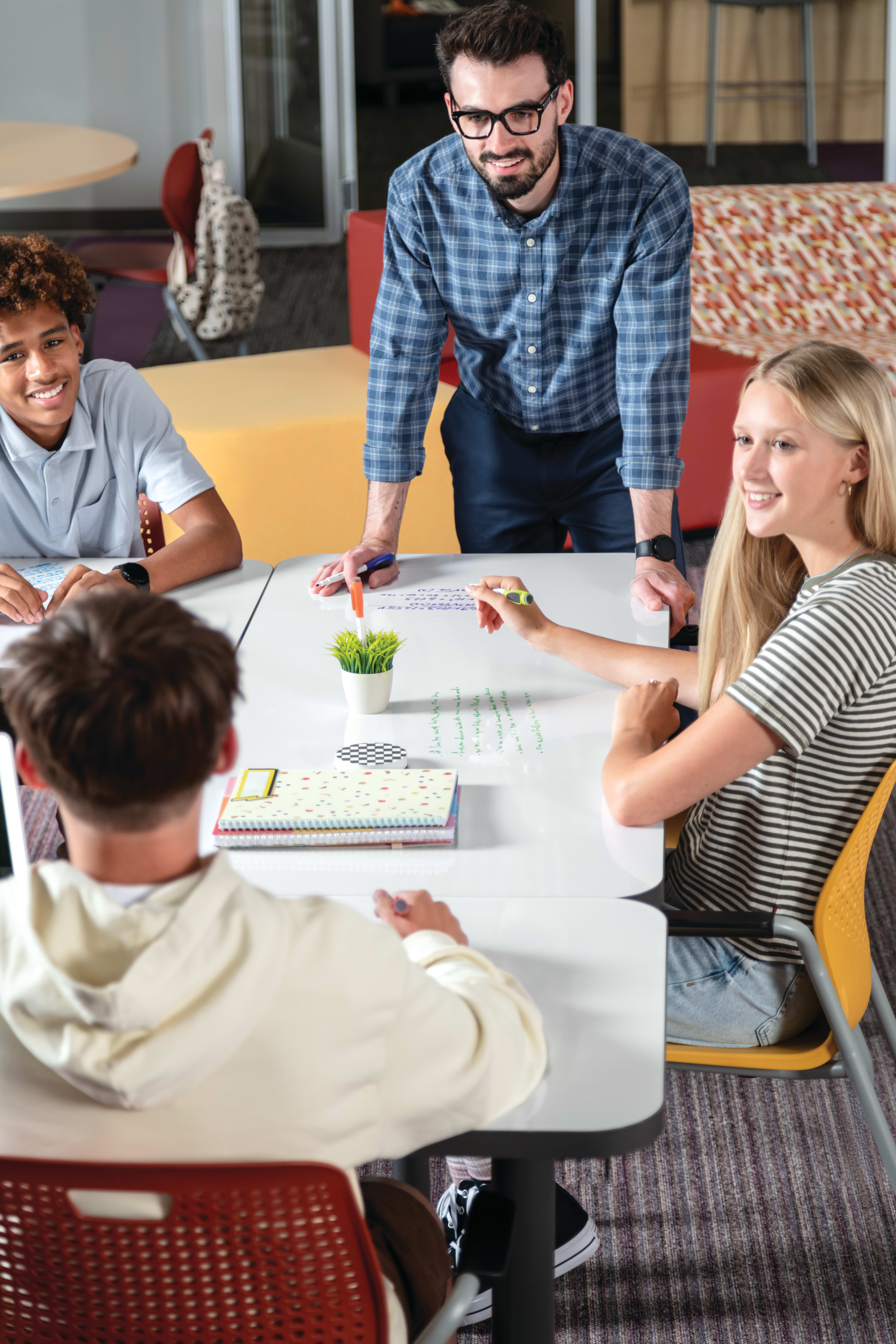 Students and teacher collaborating at Field Trip tables with red and yellow Etch chairs in a Multi-media Center with Tangram seating.