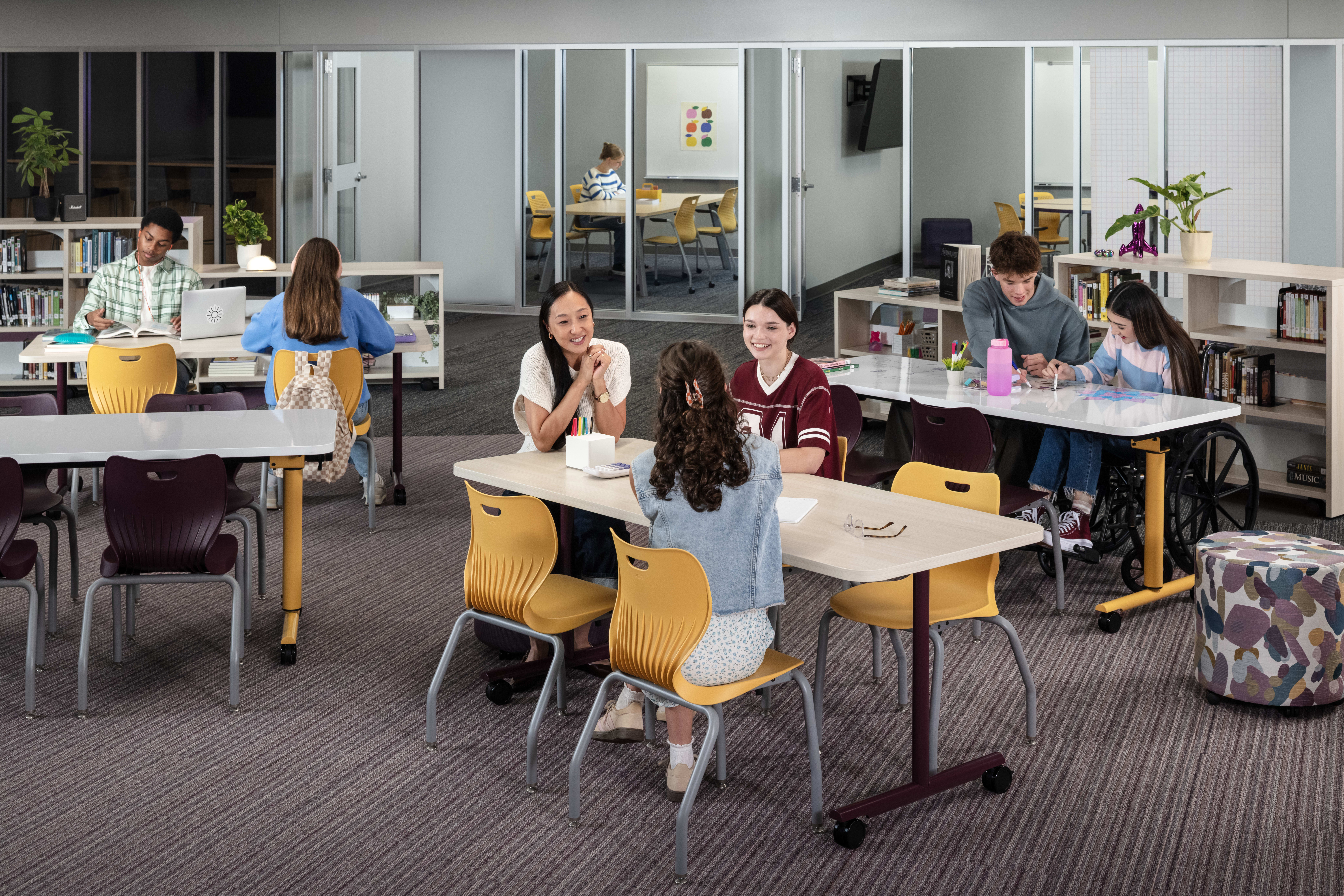 Class of students collaborating at tables in a Multi-media Center with yellow and purple product