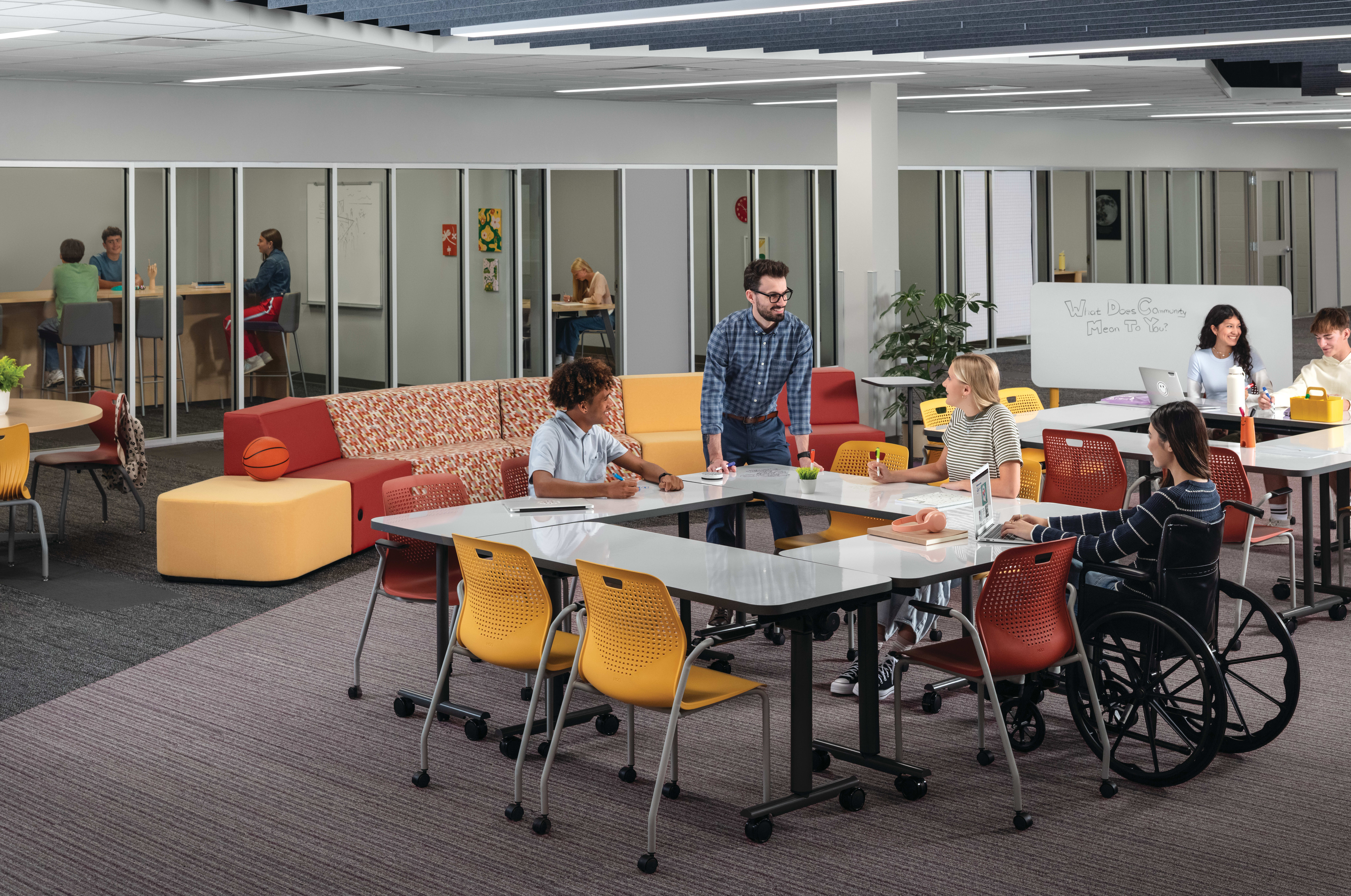 Students and teacher collaborating at Field Trip tables with red and yellow Etch chairs in a Multi-media Center with Tangram seating.