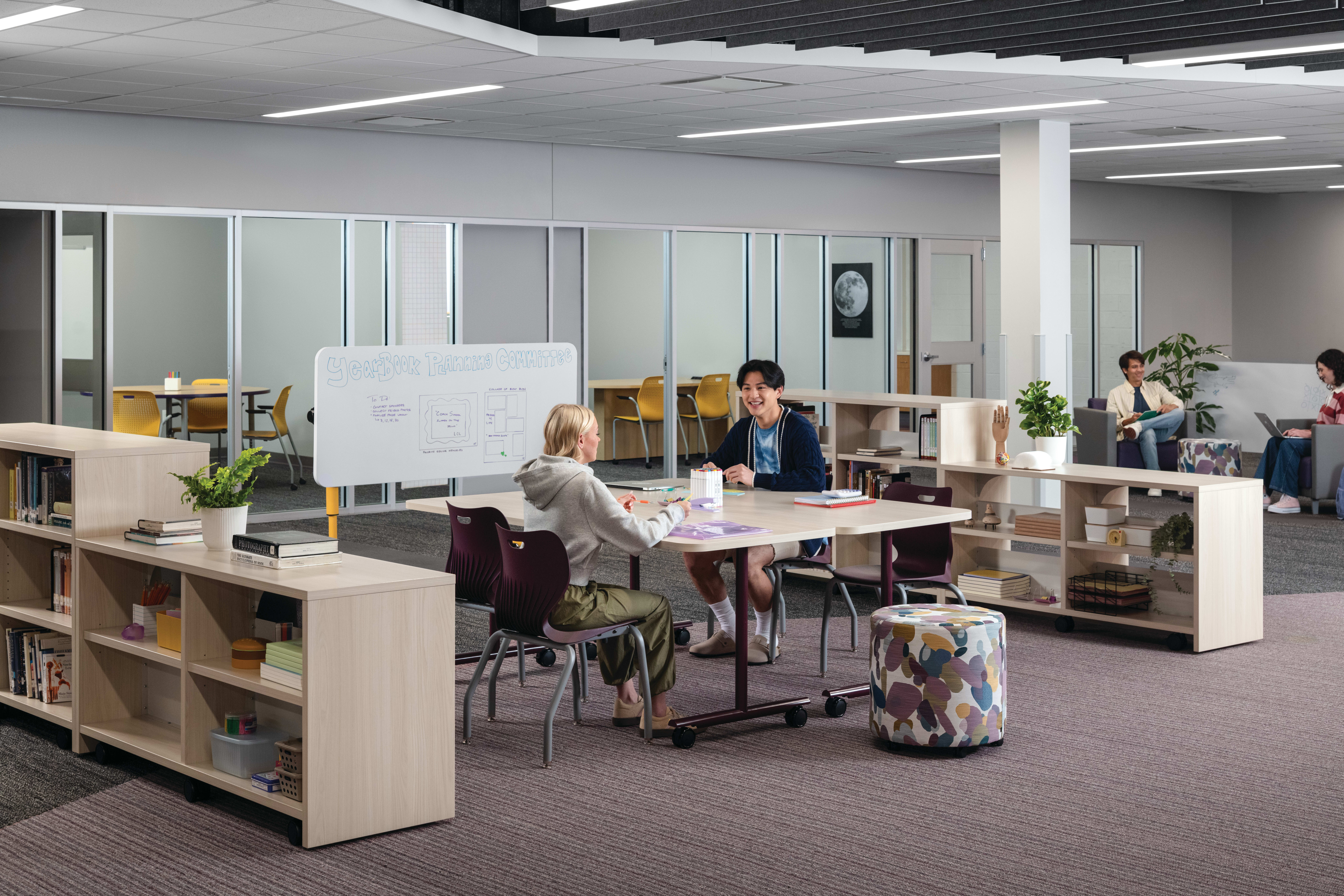 Two students collaborating at Field Trip tables with purple SmartLink chairs in a Multi-media Center with Storyline bookcases.