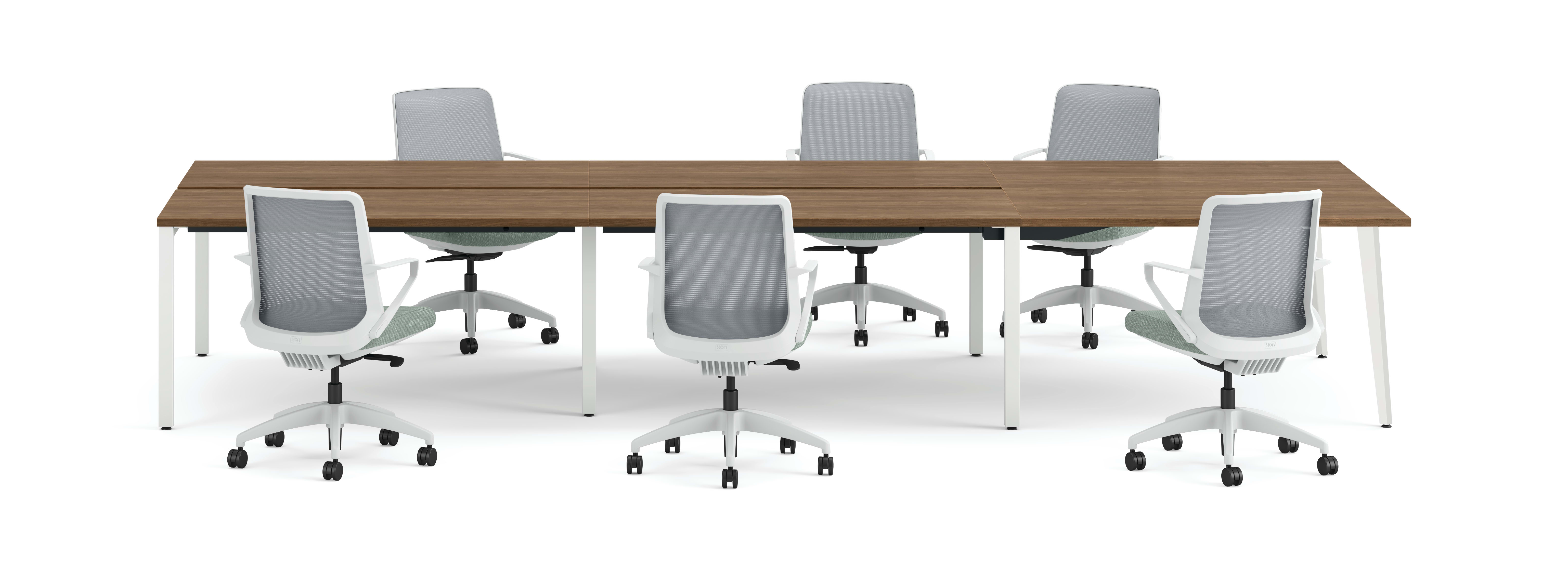 Six ergonomic office chairs arranged around two connected rectangular desks with wooden tops and white legs.