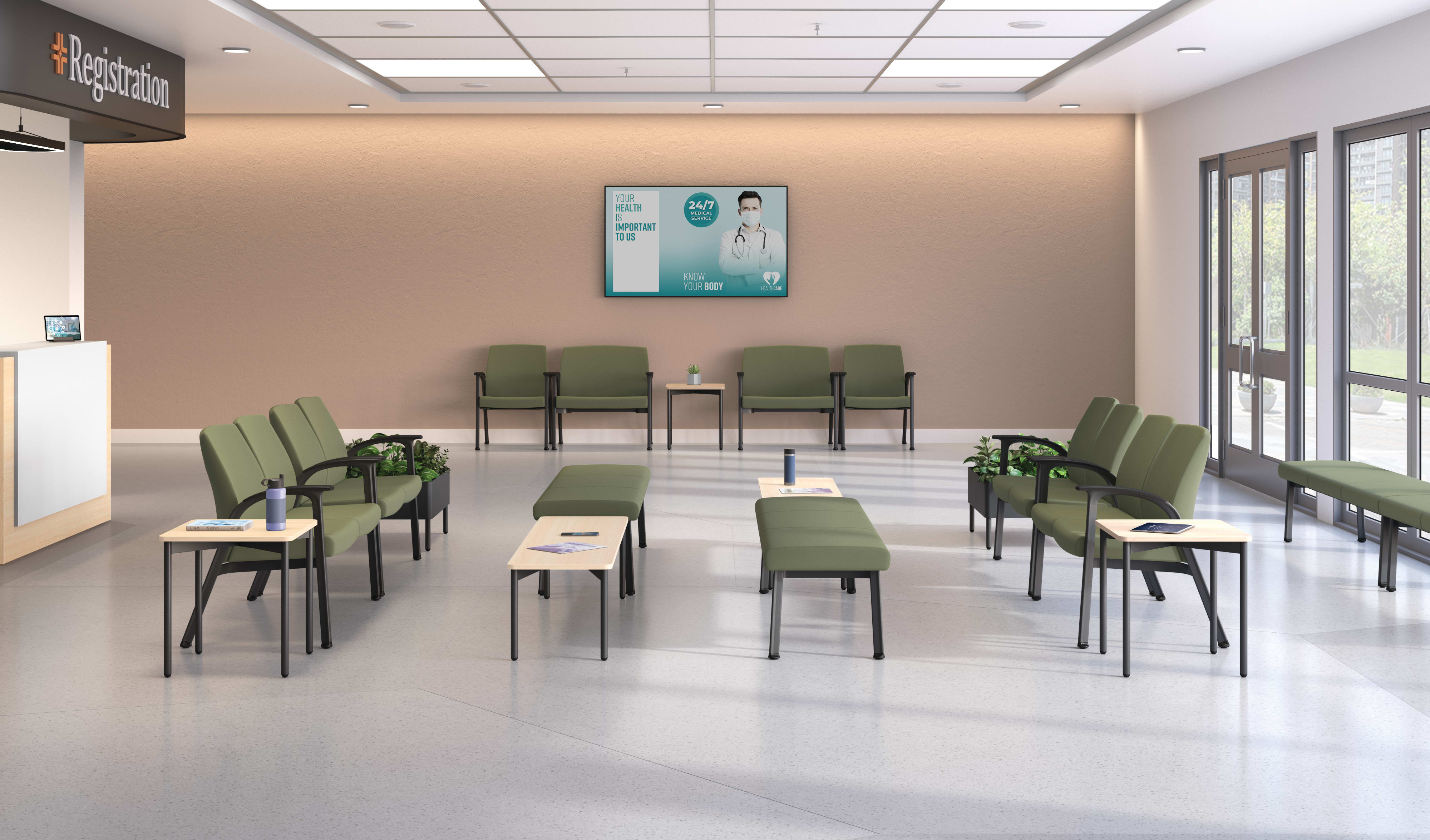 Spacious waiting area with green cushioned chairs and benches arranged around light wood tables, complemented by potted plants, a registration desk, and a wall-mounted digital display.