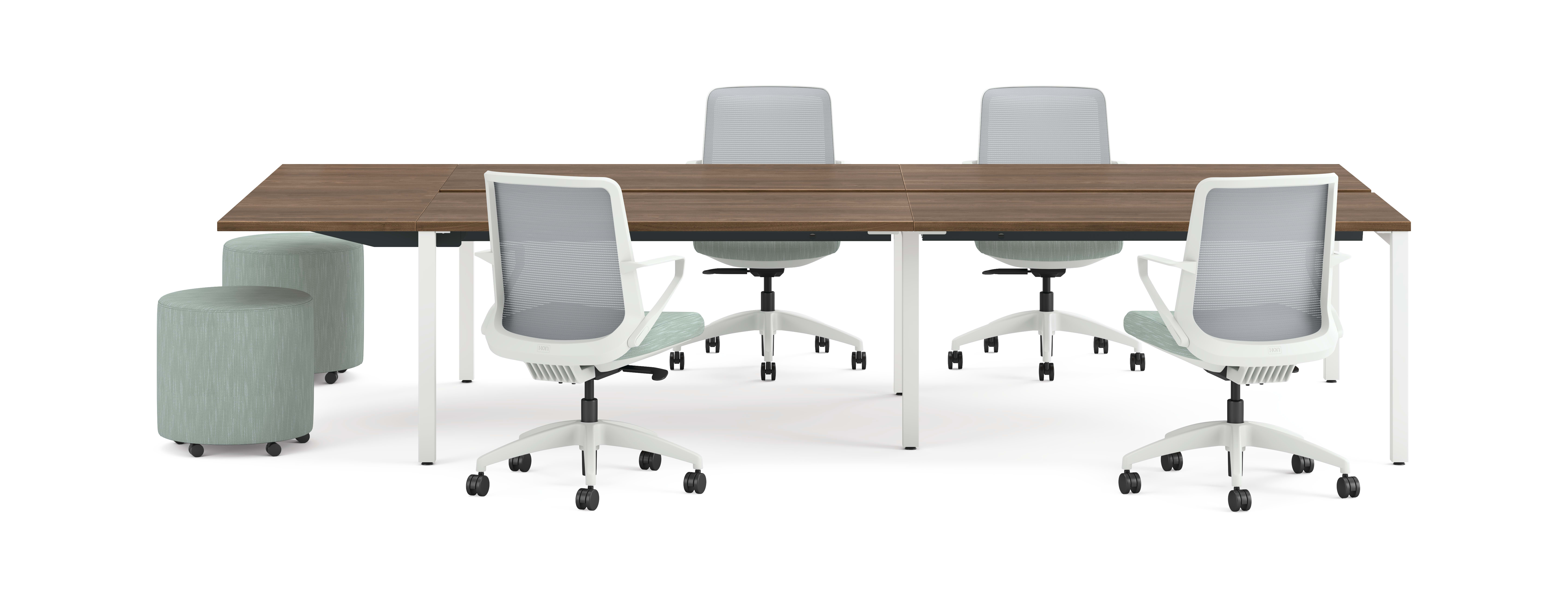 Four ergonomic office chairs around two connected rectangular desks with wooden tops and white legs, accompanied by two round upholstered stools.