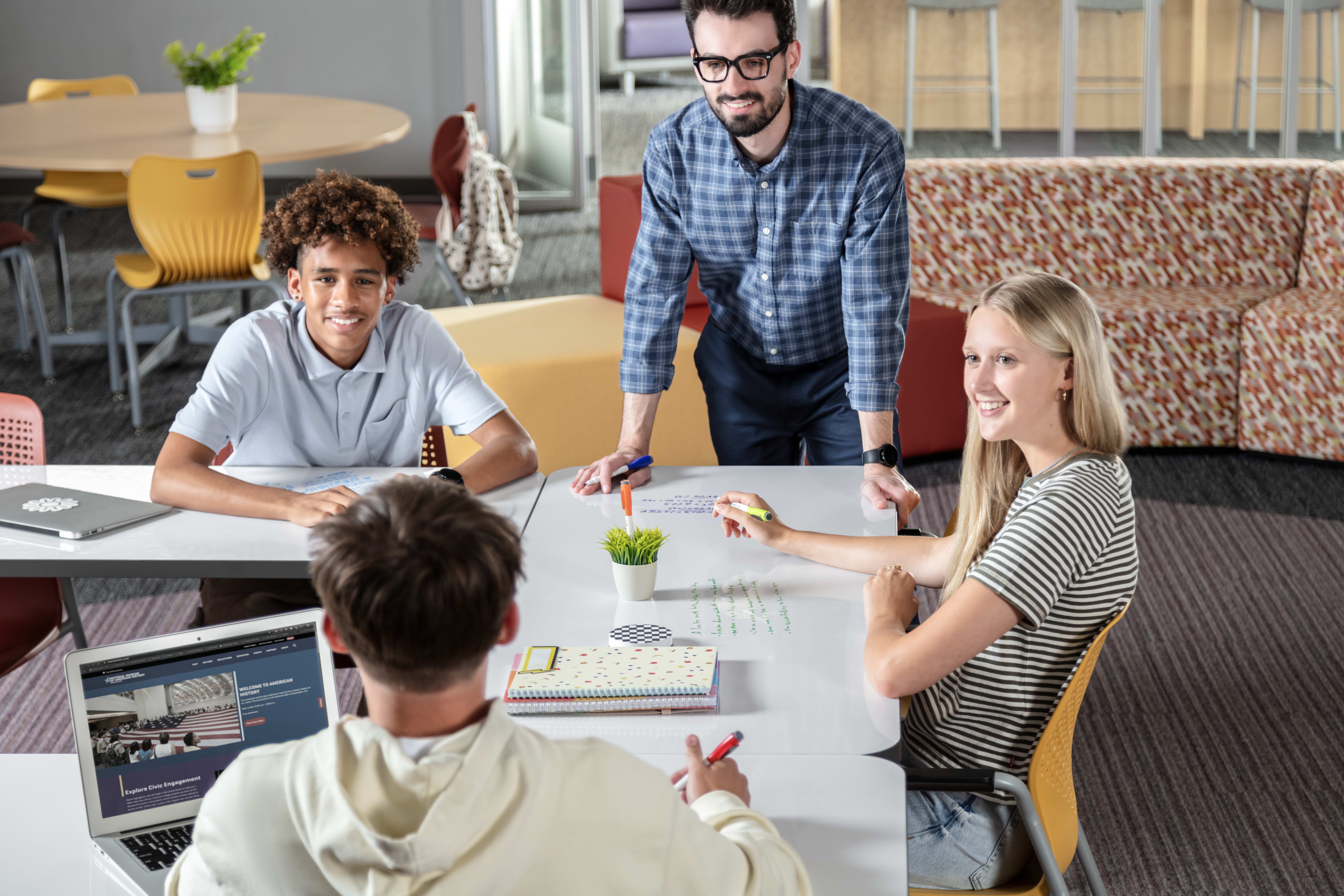 Students and a teacher collaborating in a red and yellow Multi-media Center.