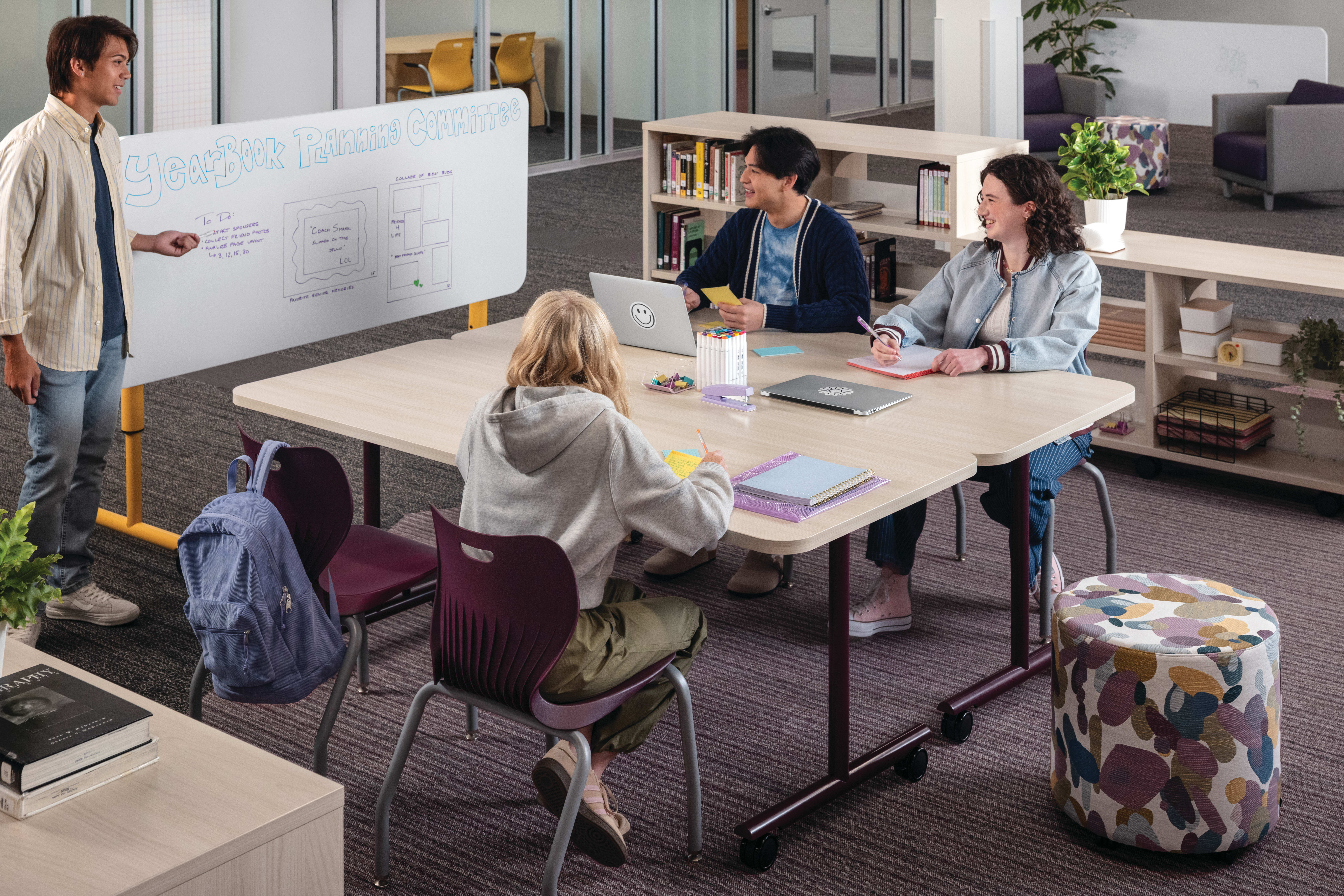 Group of students collaborating at Field Trip tables with purple SmartLink chairs in a Multi-media Center with Storyline bookcases.