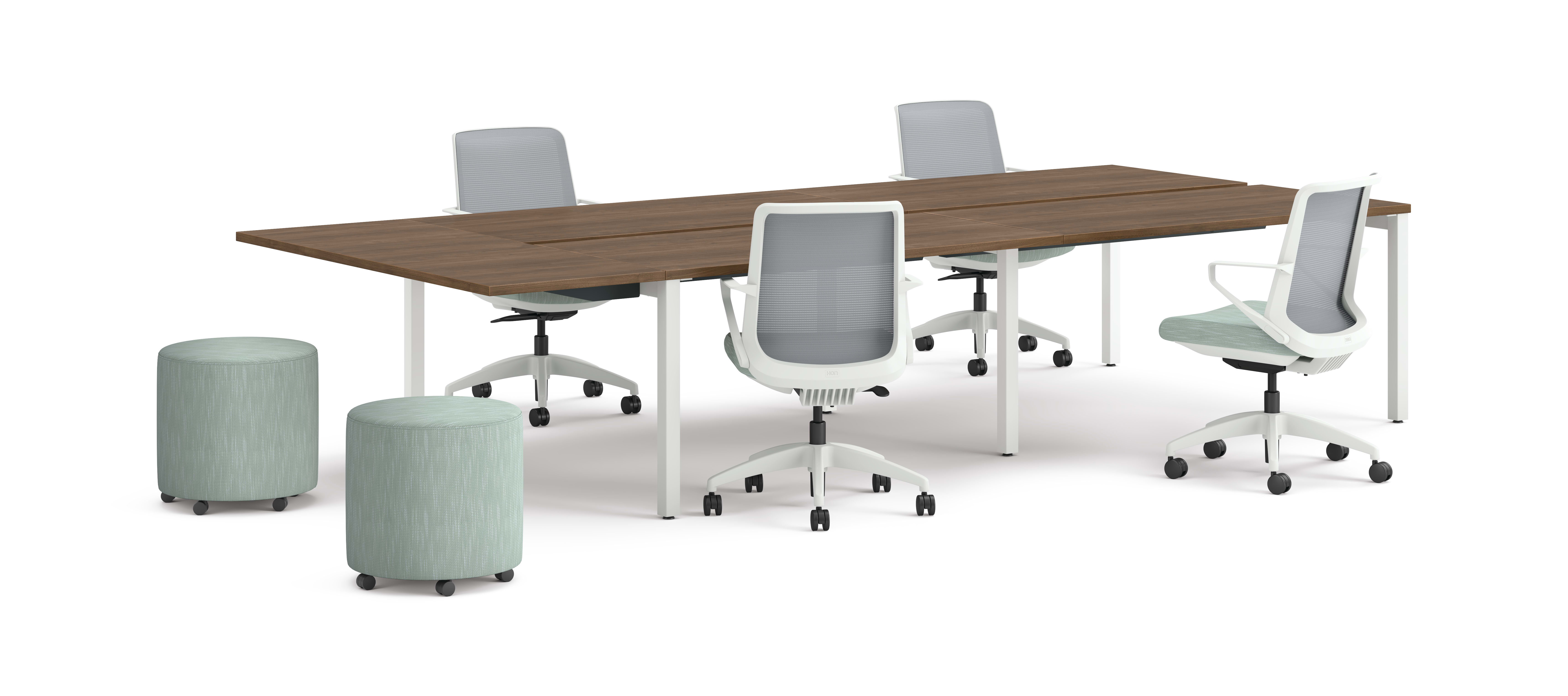 Four ergonomic office chairs around two connected rectangular desks with wooden tops and white legs, accompanied by two round upholstered stools.