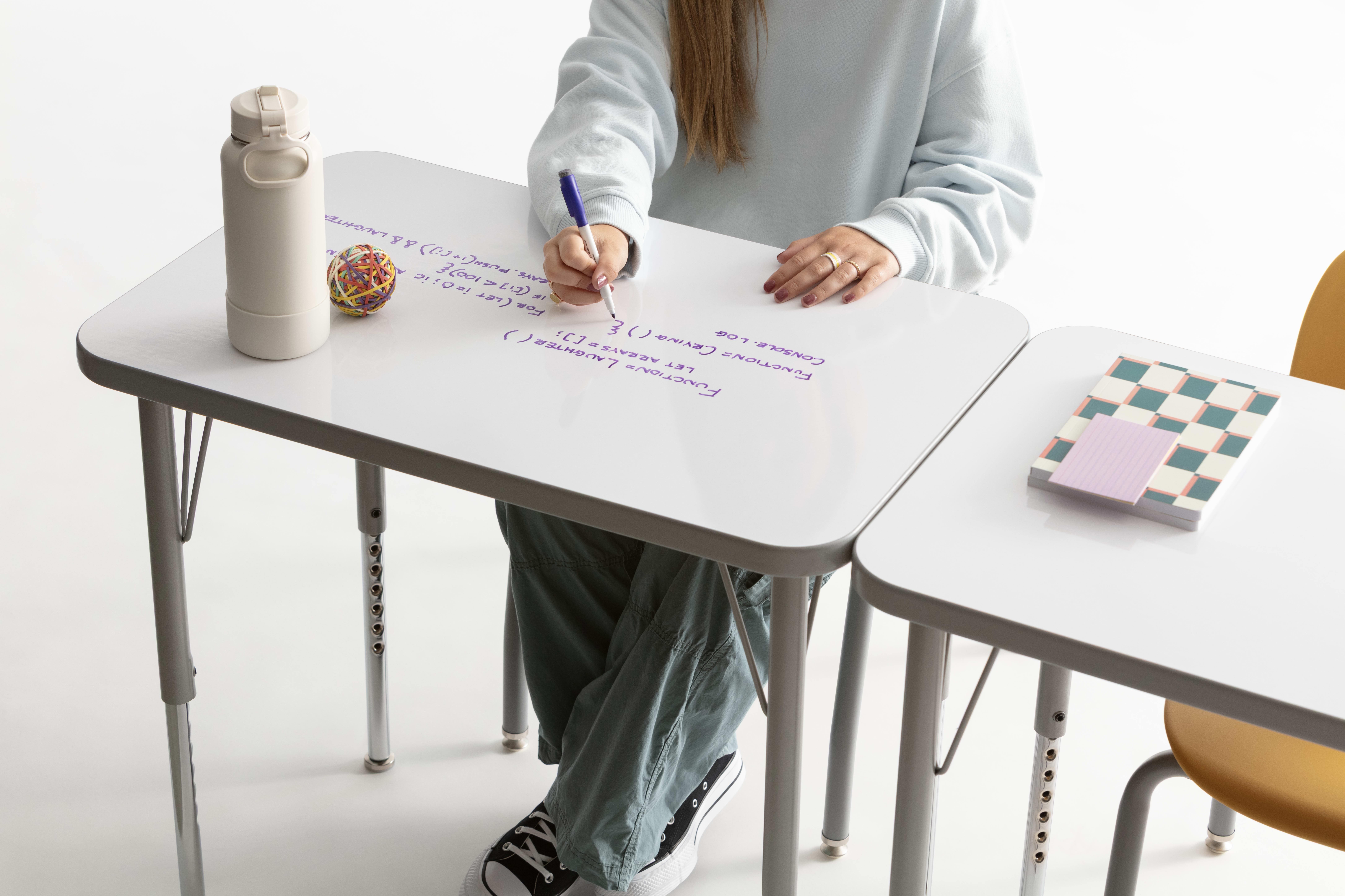 One student writing on the whiteboard top of a Build rectangle top desk.