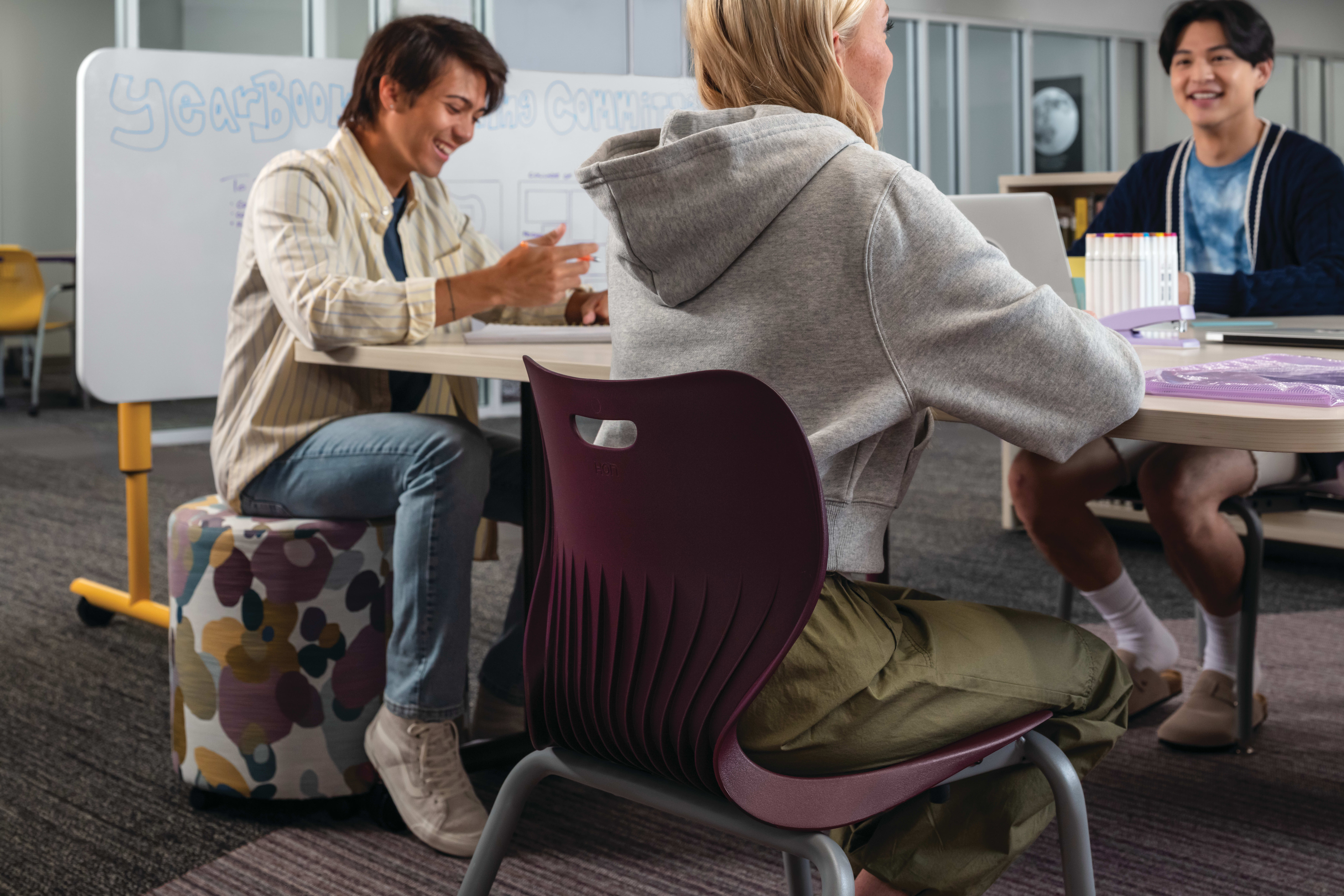 Group of students collaborating at Field Trip tables with purple SmartLink chairs in a Multi-media Center with Storyline bookcases.
