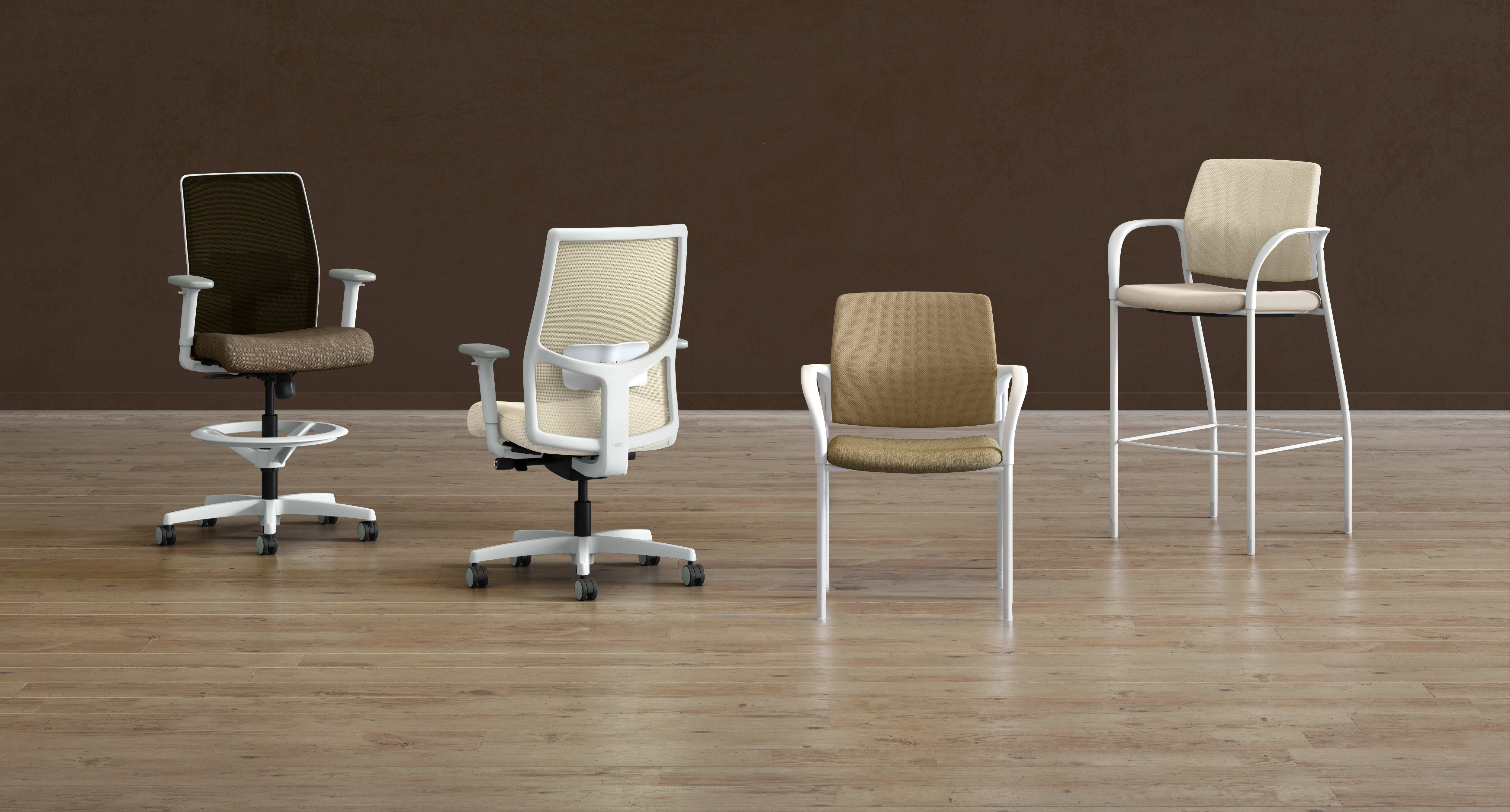 A collection of modern office chairs in various styles and colors, arranged on a wooden floor against a plain brown background.