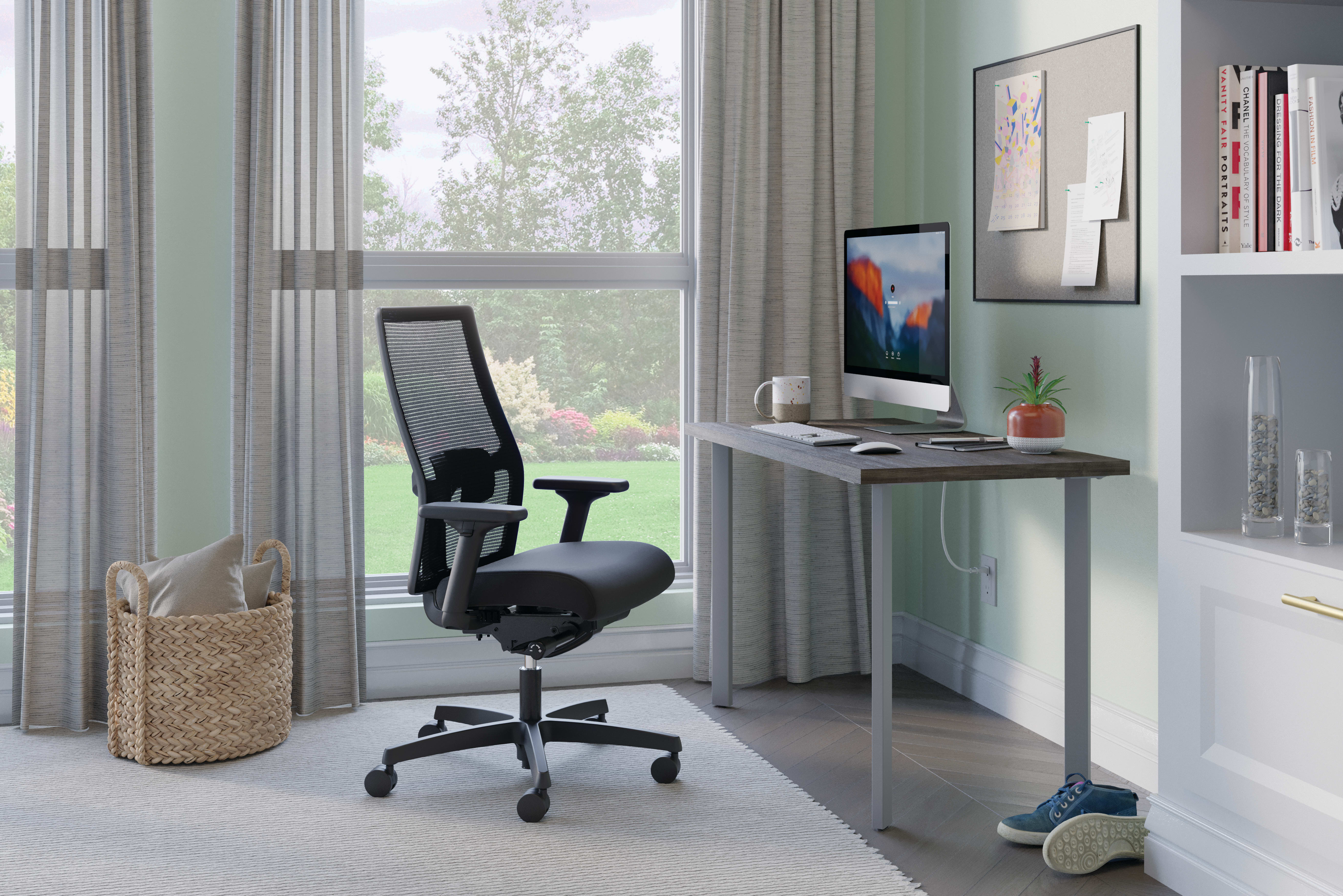 A modern and minimalist home office setup with a comfortable office chair, a desk with a computer monitor, and various decor elements such as artwork and plants, all set against a large window overlooking a natural outdoor scene.