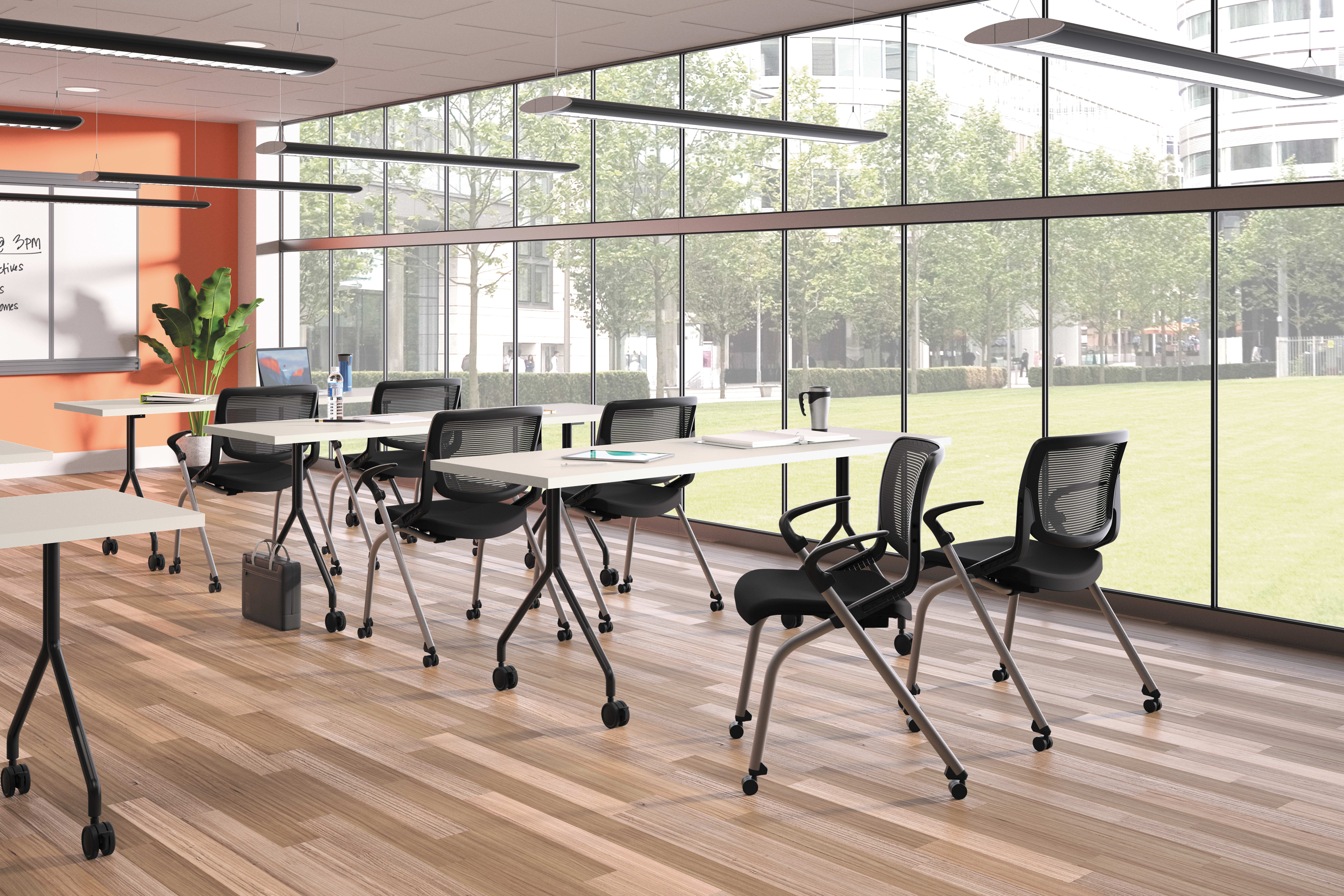 A modern, well-lit classroom with rows of desks and chairs, large windows overlooking a grassy outdoor area, and various lighting fixtures and equipment visible.