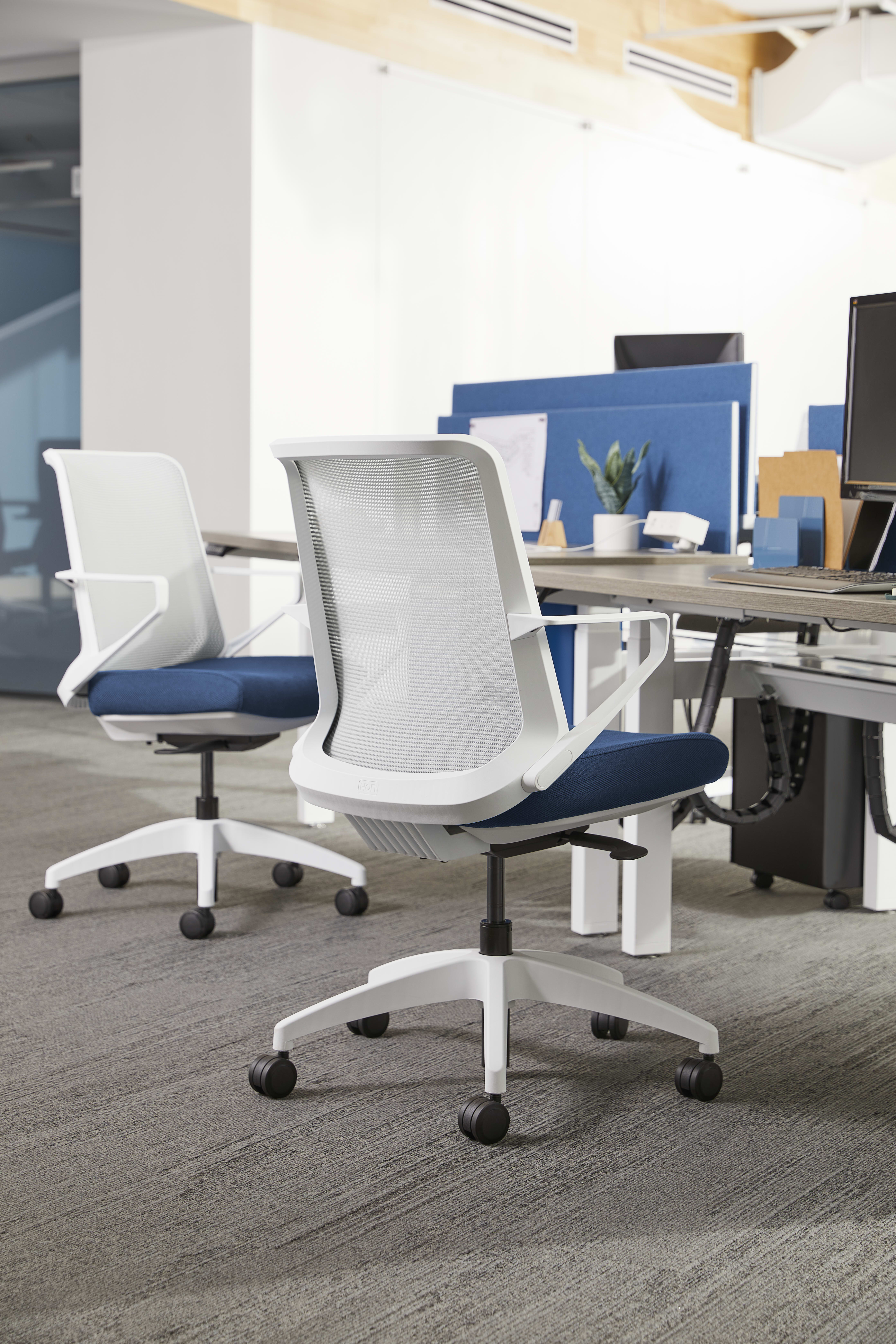 The image shows a modern office space with white and blue office chairs arranged around a table, with shelves and other office equipment visible in the background.
