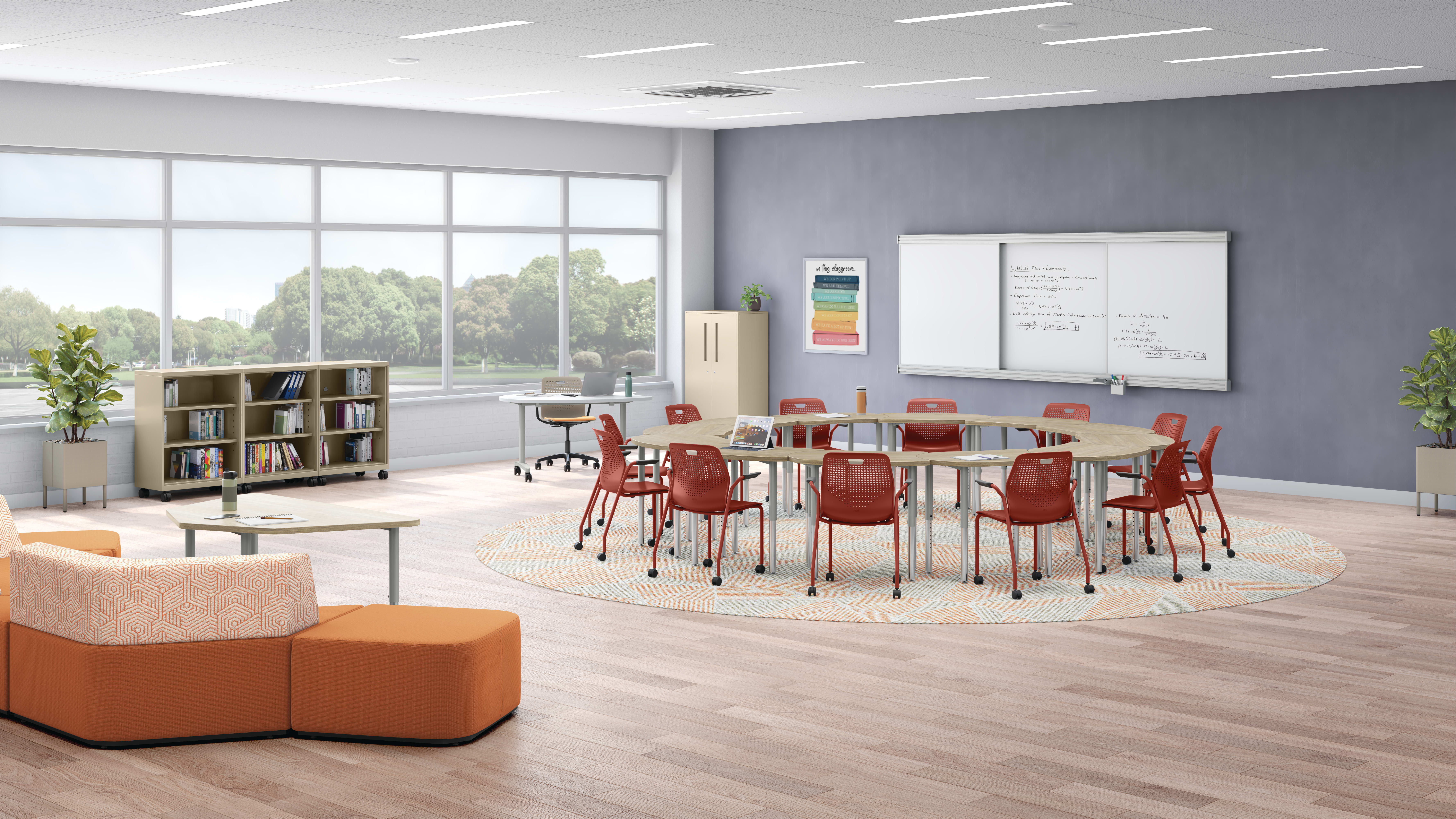 A modern, well-lit classroom with a large table surrounded by red chairs, bookshelves, and a whiteboard on the wall. The room has large windows overlooking a scenic outdoor area.
