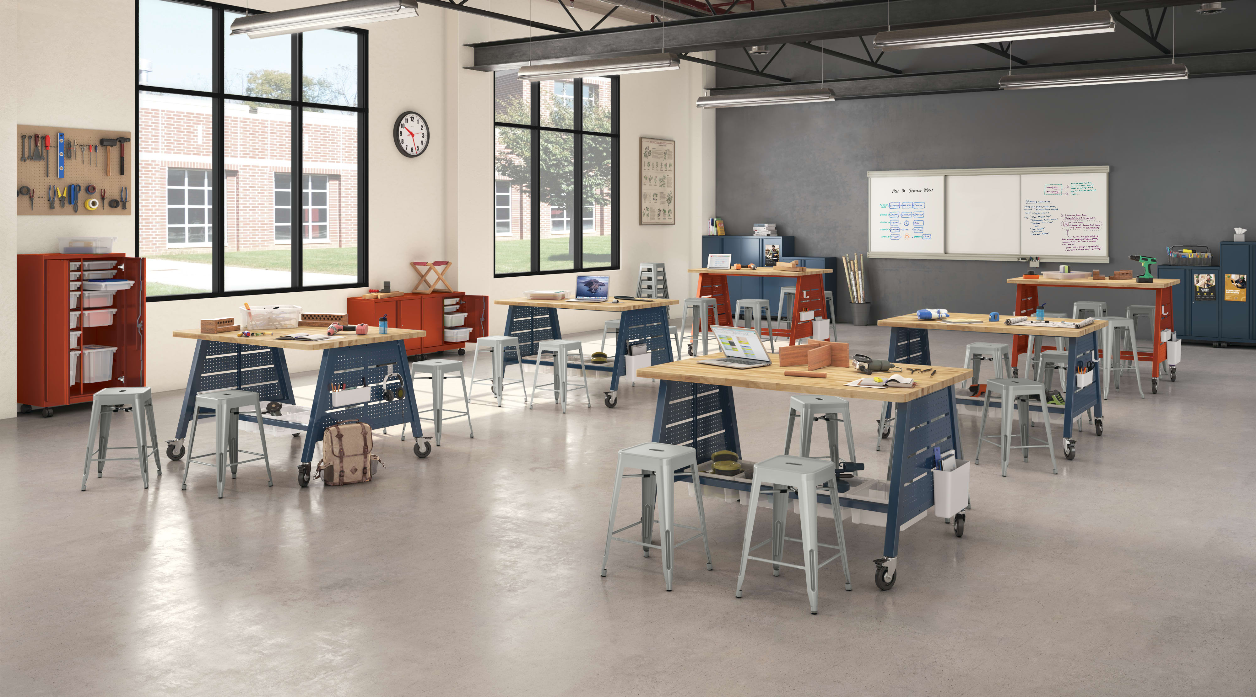 A modern, open-concept workspace with various workstations, desks, and chairs arranged throughout the room. The space features large windows, exposed ceiling beams, and a whiteboard on the wall, creating a bright and collaborative environment.