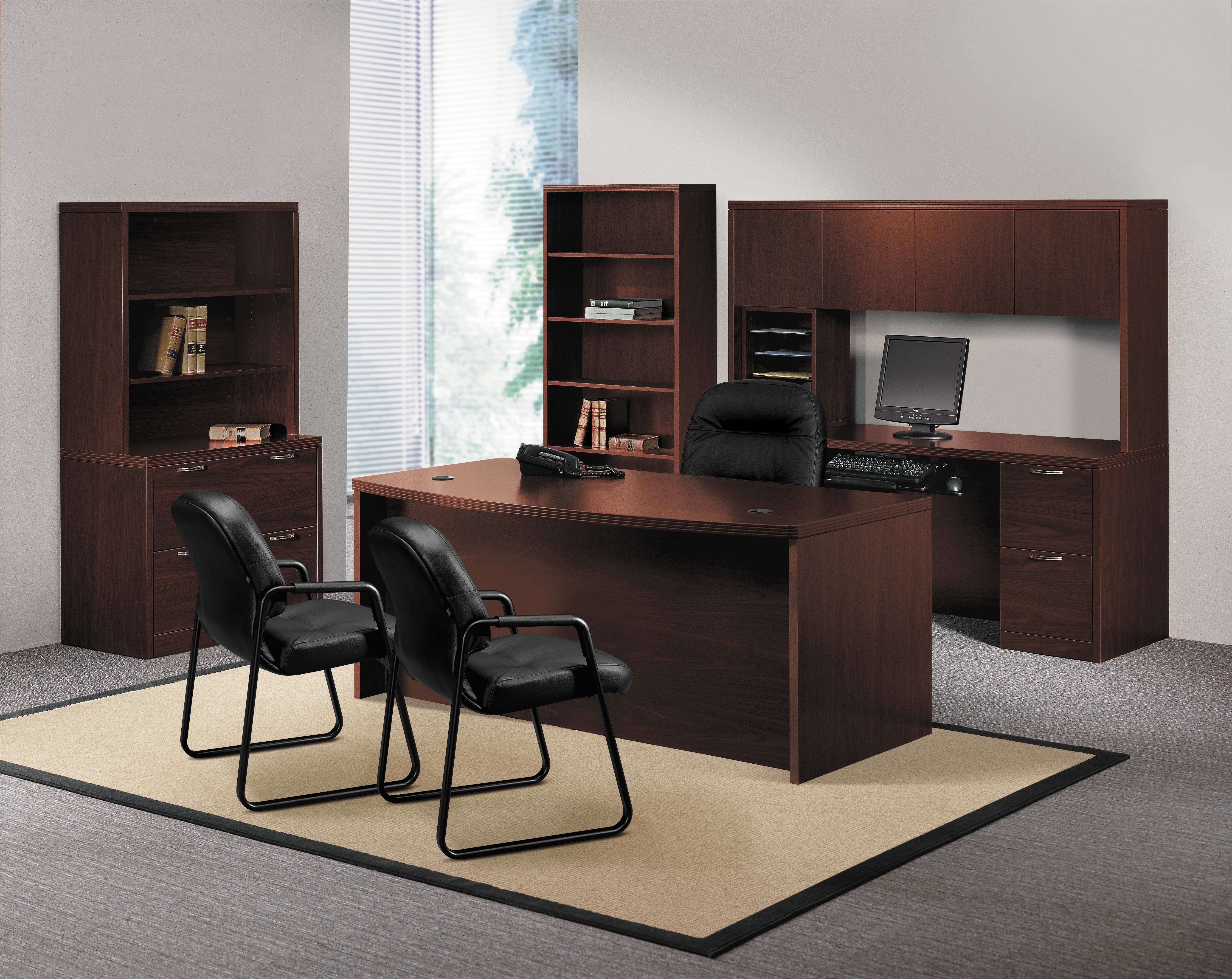 A modern and minimalist home office setup with a large wooden desk, bookshelves, and black office chairs arranged in a spacious room with a large window providing natural lighting.