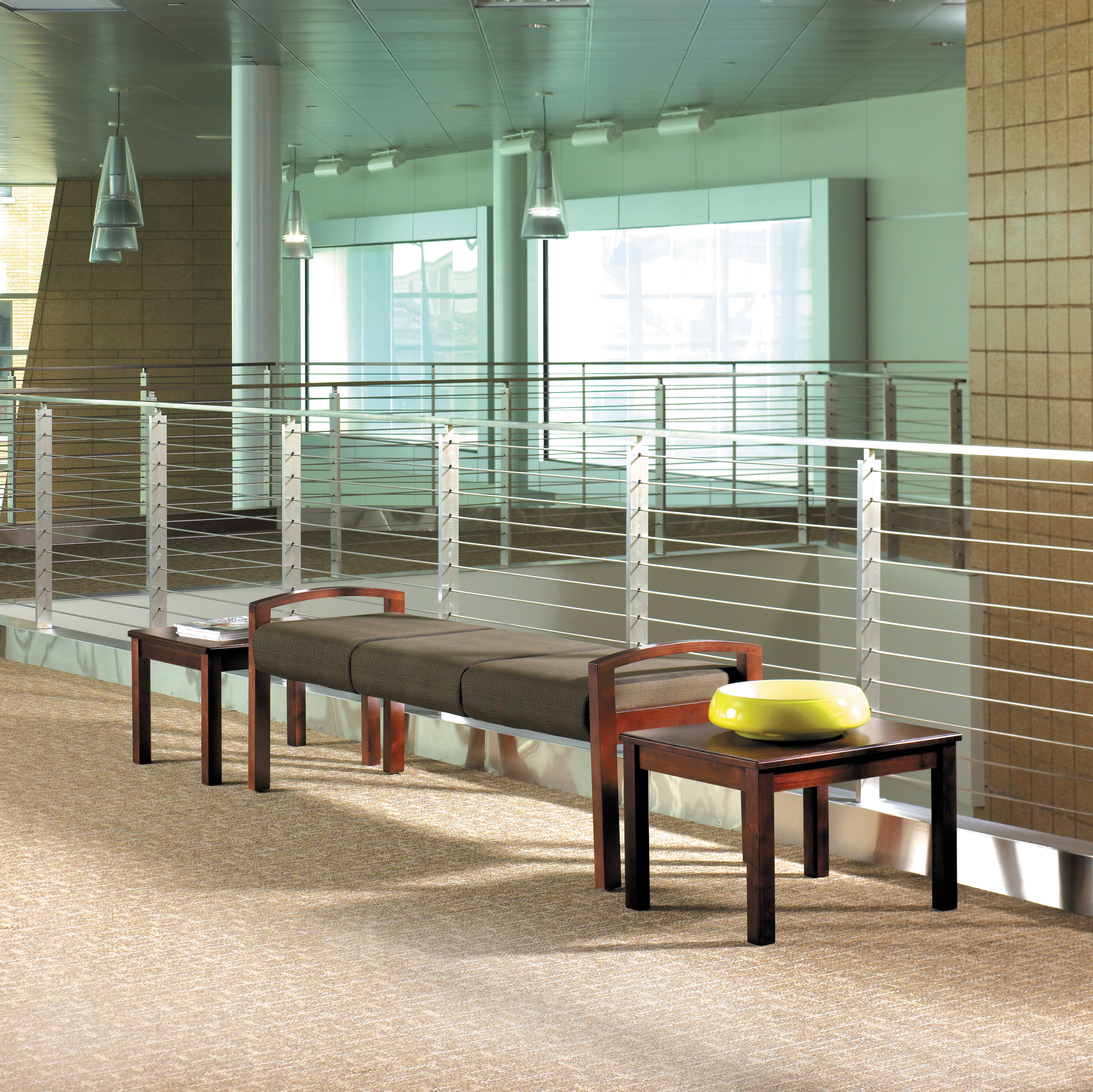 The image shows a modern, minimalist interior space with wooden benches and colorful cushions in the foreground, and a glass wall with metal railings in the background.