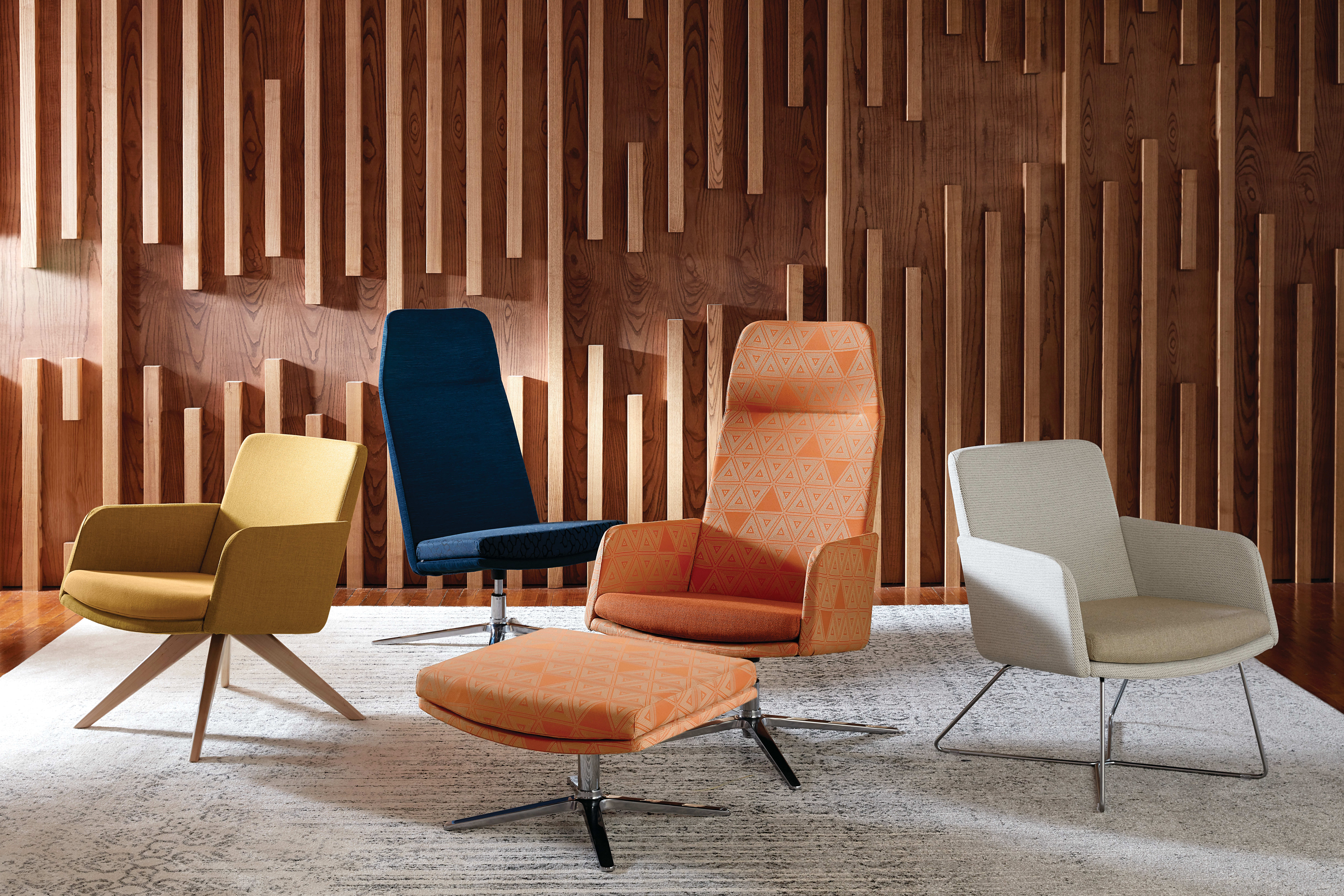 A collection of modern, colorful chairs and ottomans arranged in a room with a striking wooden wall feature.