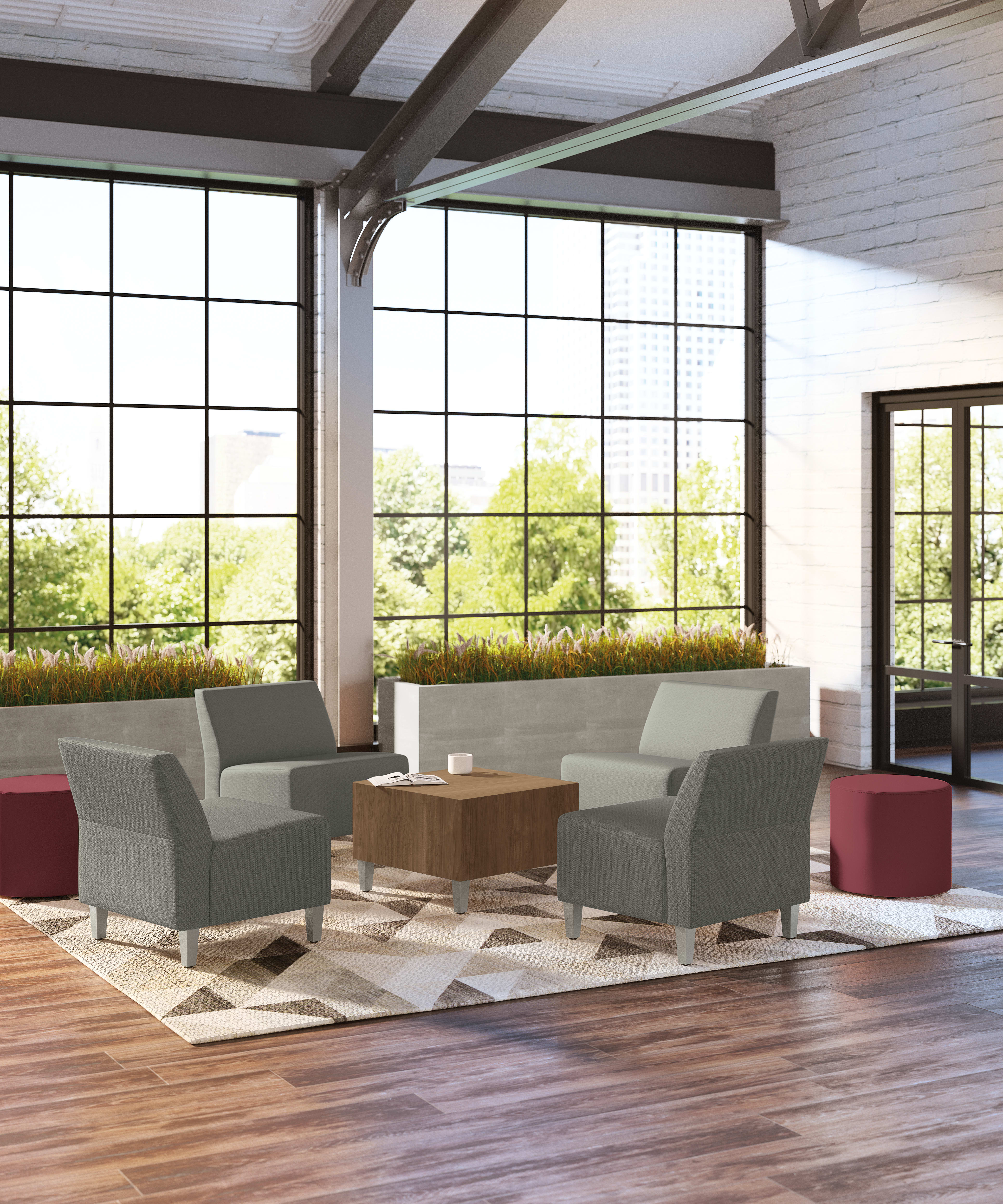 A modern and spacious living room with large windows overlooking a lush outdoor landscape, featuring comfortable gray armchairs, a wooden coffee table, and a patterned area rug on the hardwood floor.