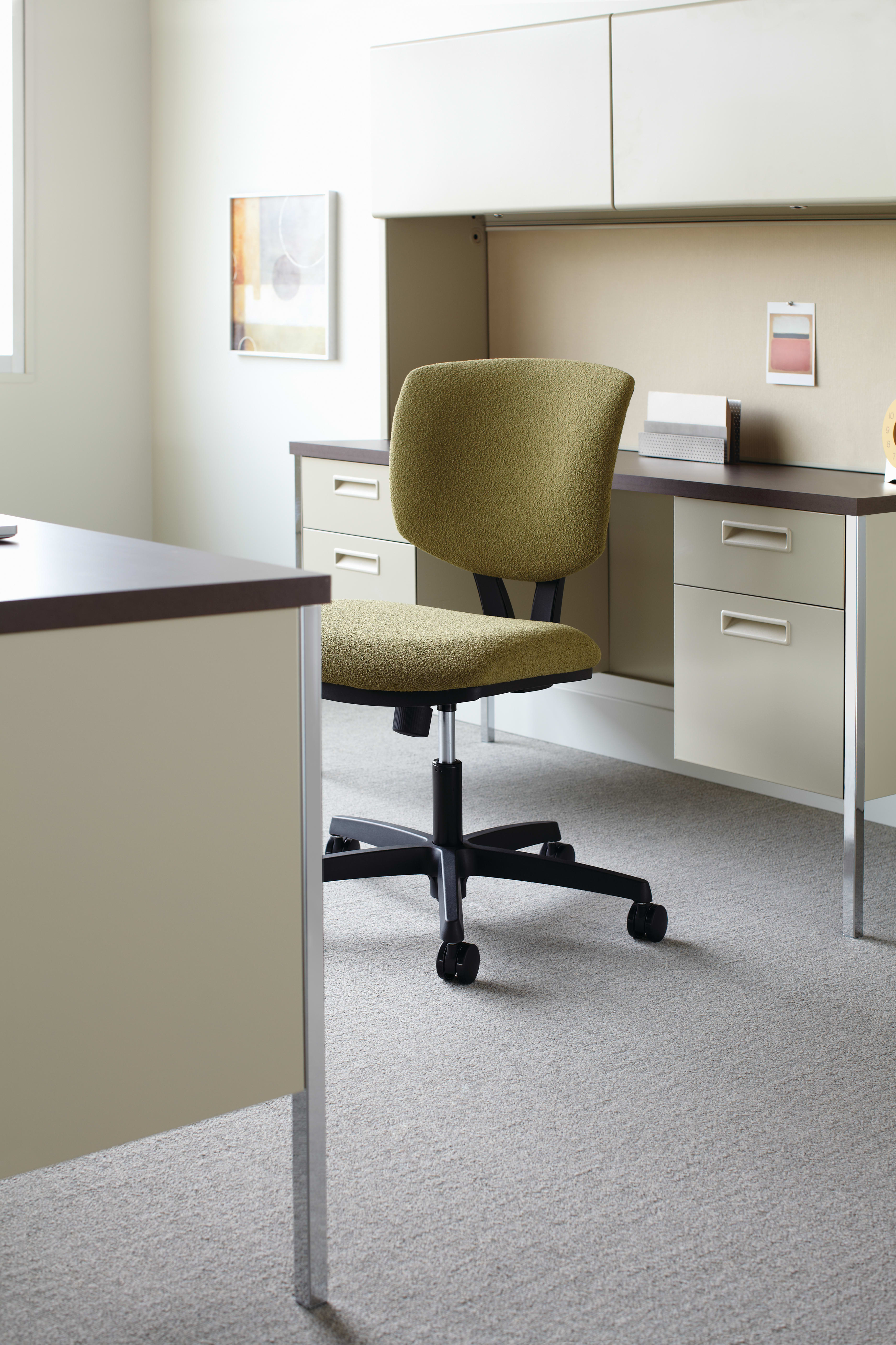 The image depicts an office workspace with a desk, a green upholstered office chair, and various storage units in the background.