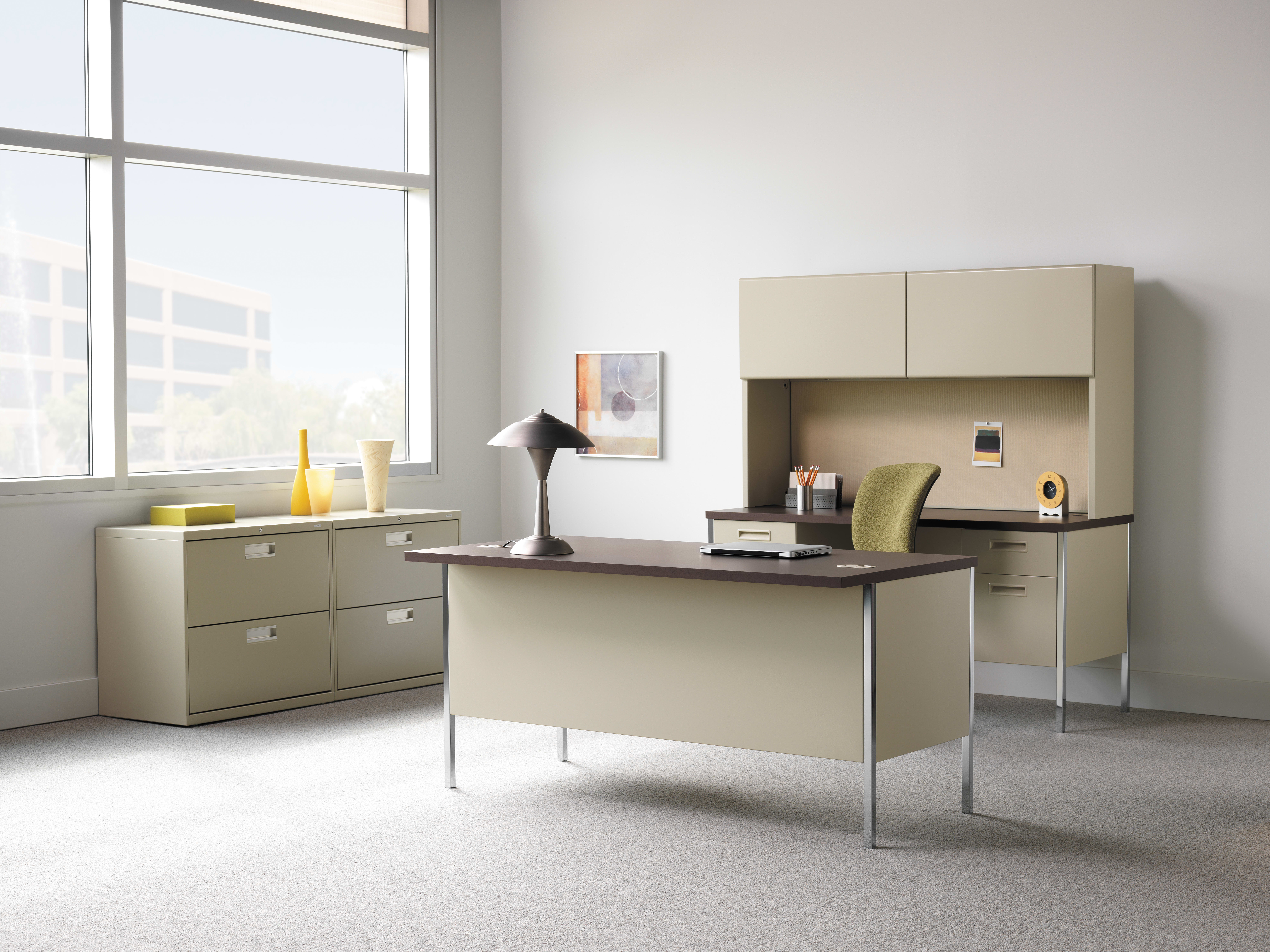 A modern, minimalist office space with a desk, storage cabinets, and a large window providing natural light.