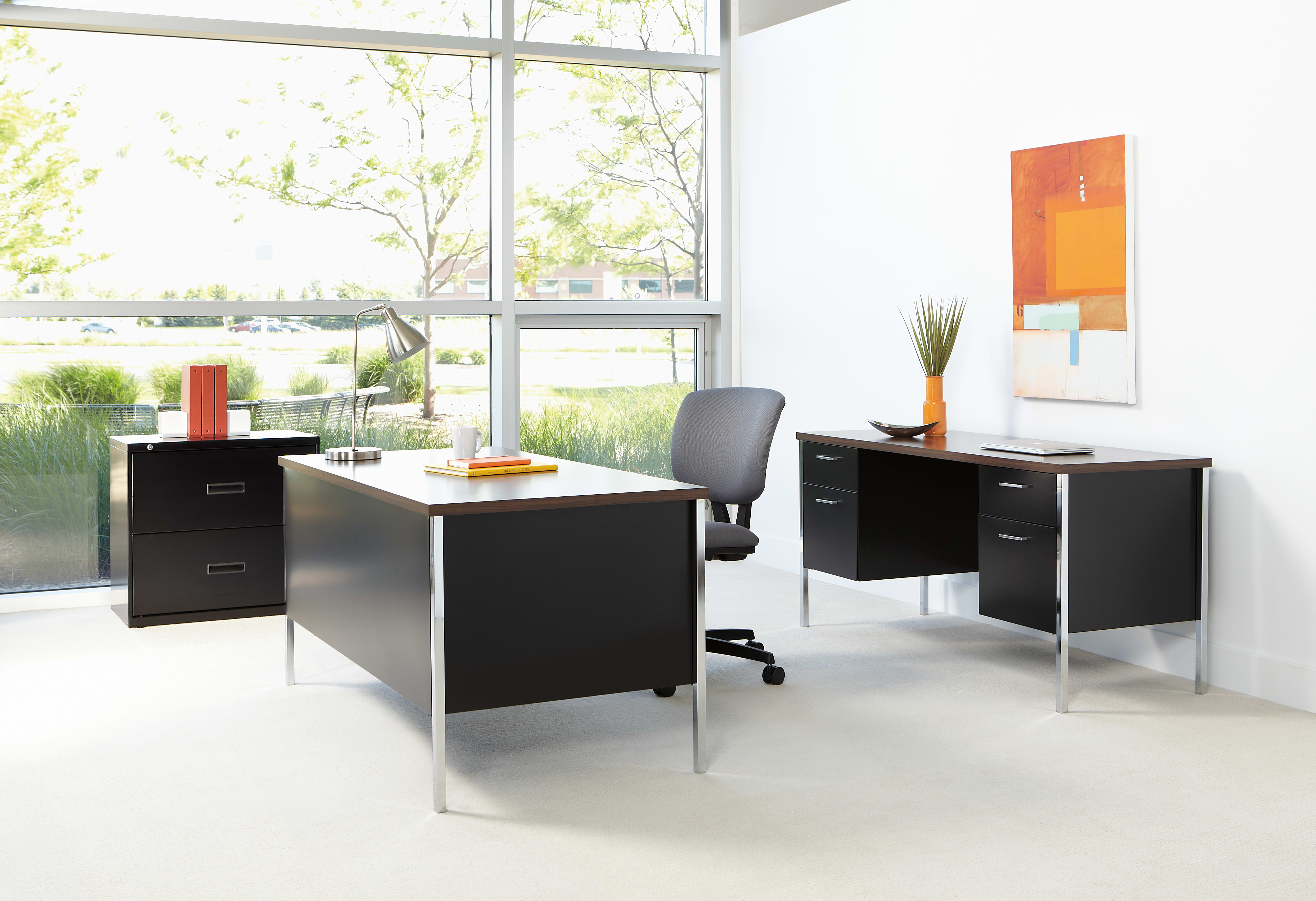 A modern and minimalist office space with sleek black furniture, large windows overlooking greenery, and vibrant artwork on the walls.