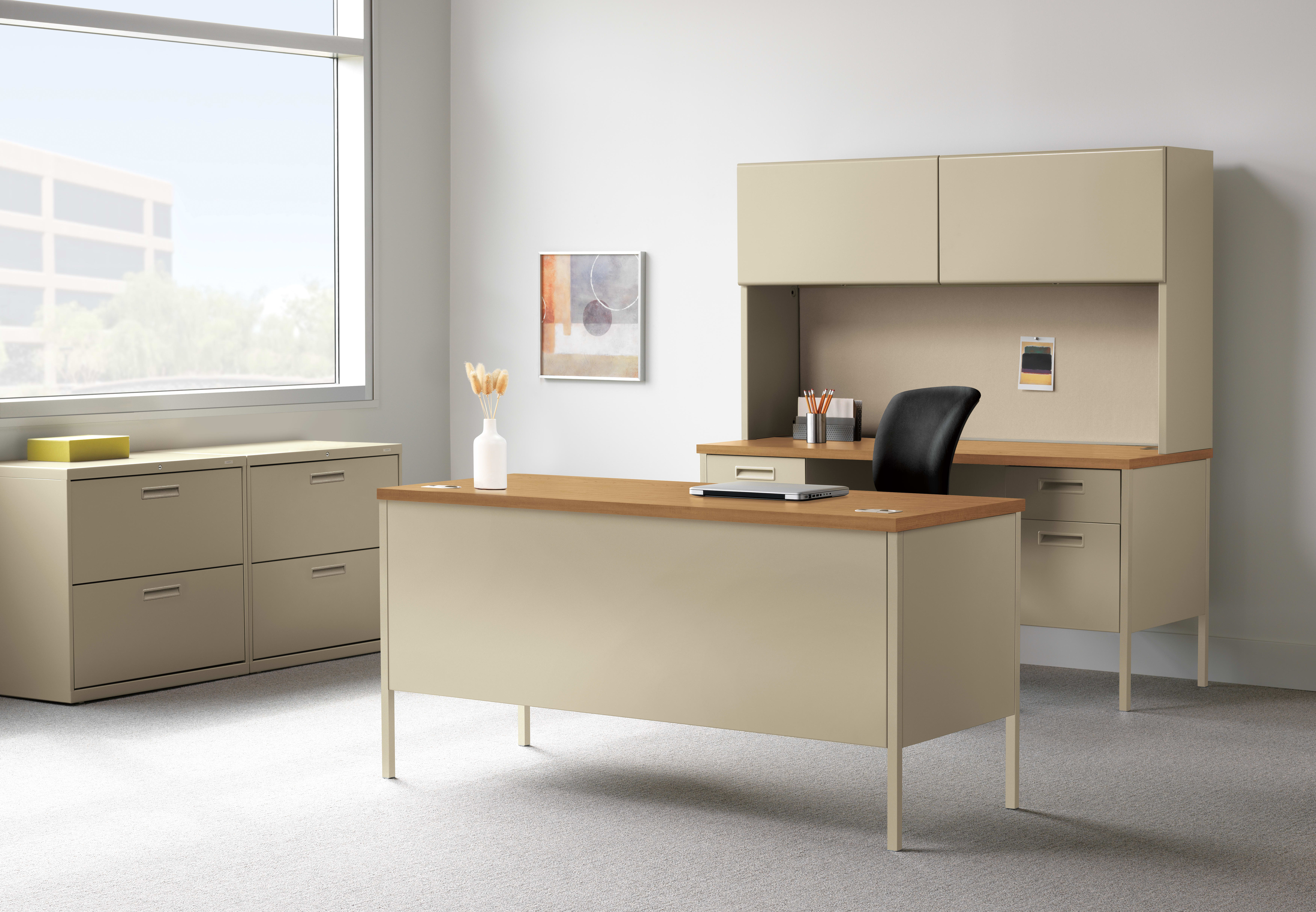 A modern and minimalist office space with a wooden desk, beige cabinets, and a large window providing natural light.