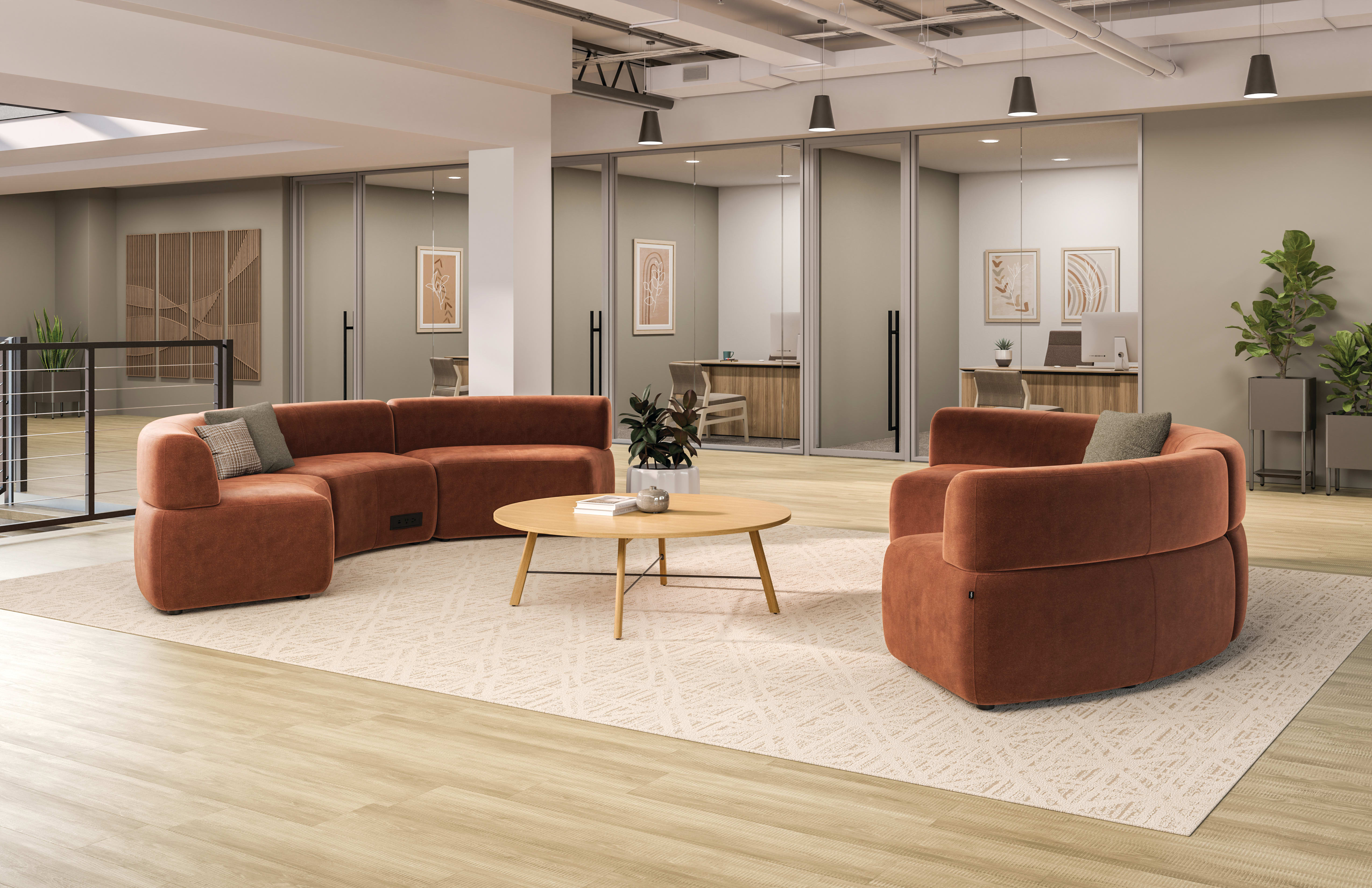 Modern office lounge with rust-colored sectional sofas, rounded armchairs, a light wood coffee table, and a neutral area rug set within an open space featuring glass-walled private offices and soft ambient lighting.
