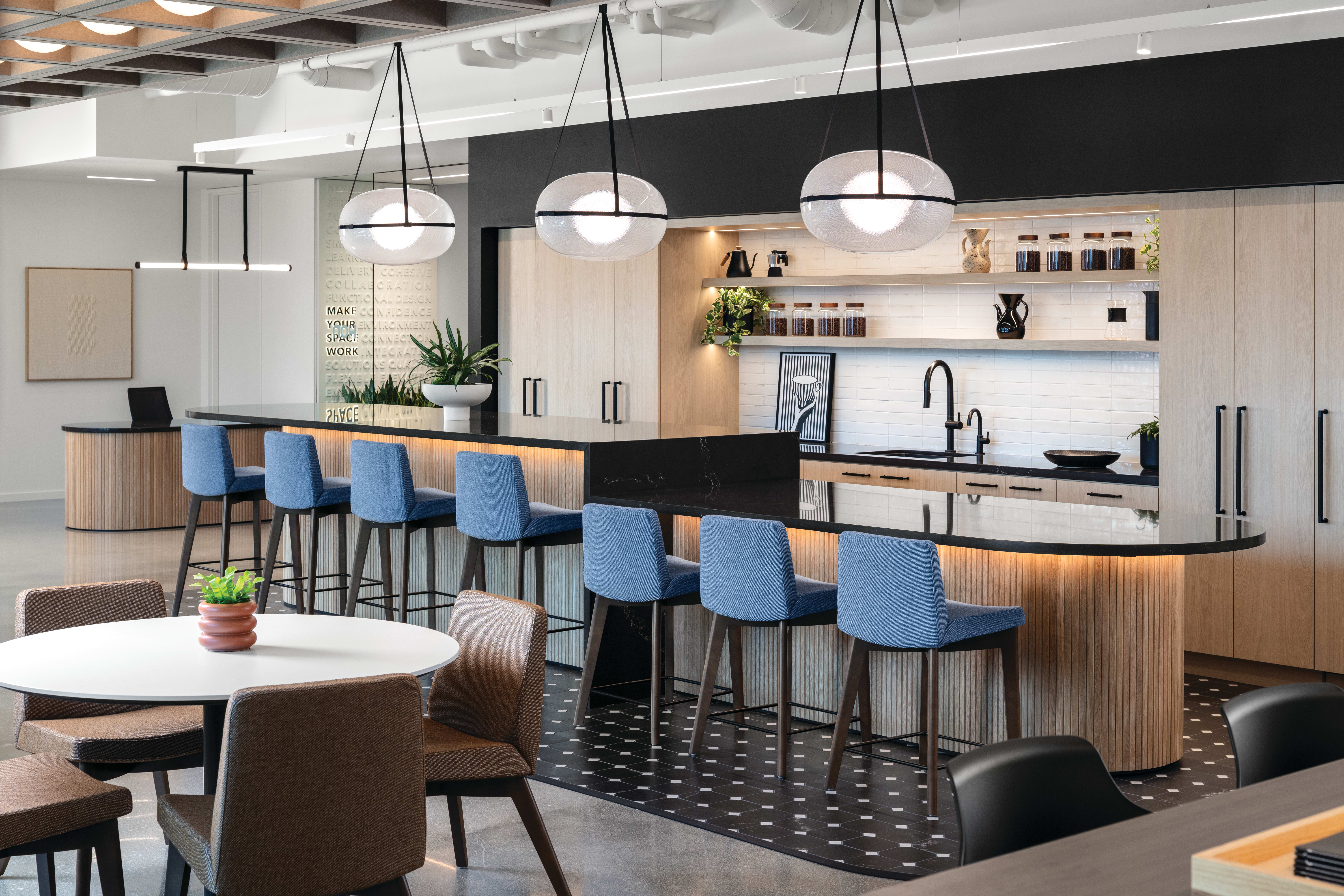 Round meeting table with upholstered guest chairs and adjacent counter-height chairs on wood legs, featuring cushioned seats and backs for collaborative seating.