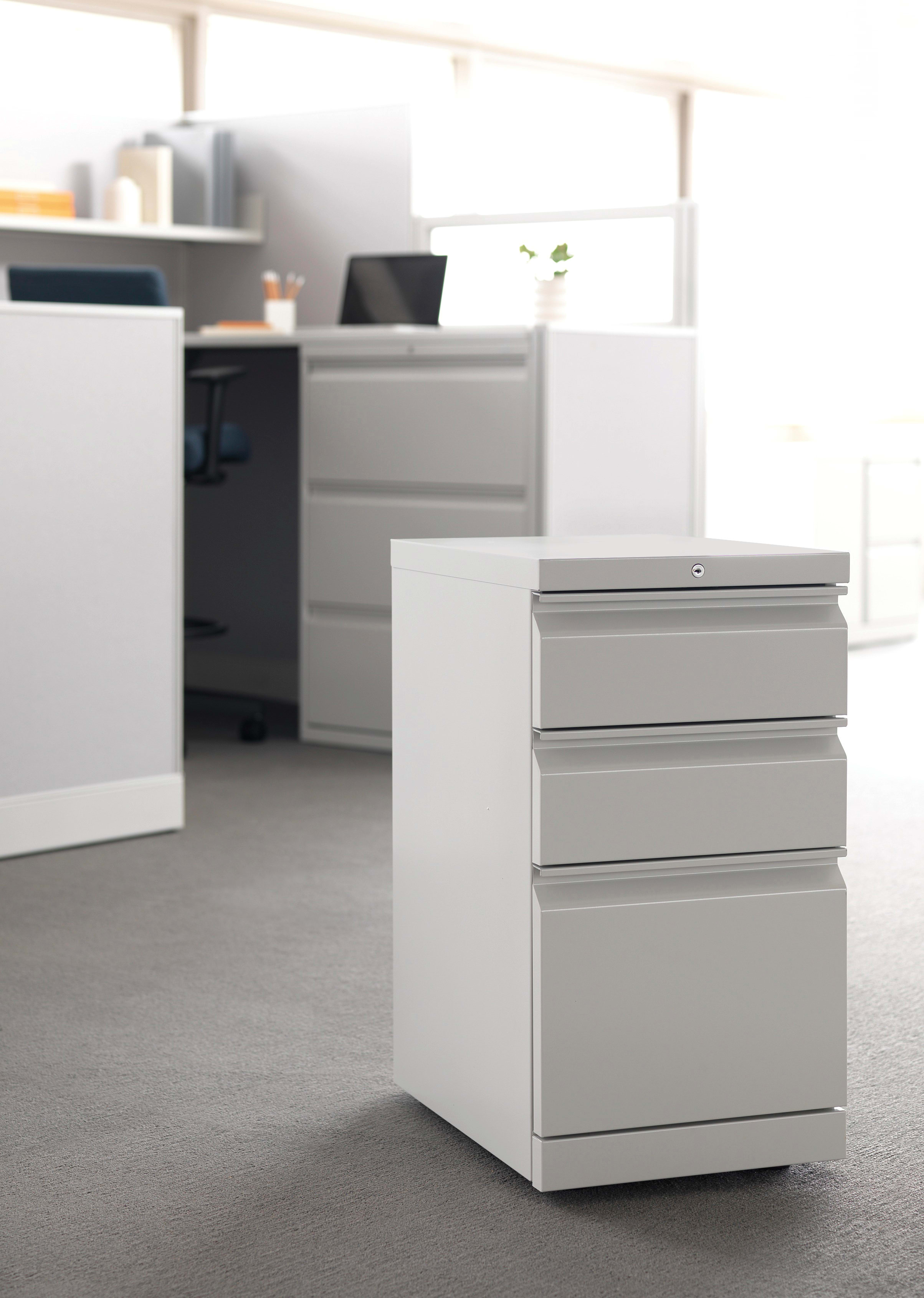 The image depicts a modern, minimalist office space with white furniture and drawers in the foreground, and a blurred background of additional office equipment.