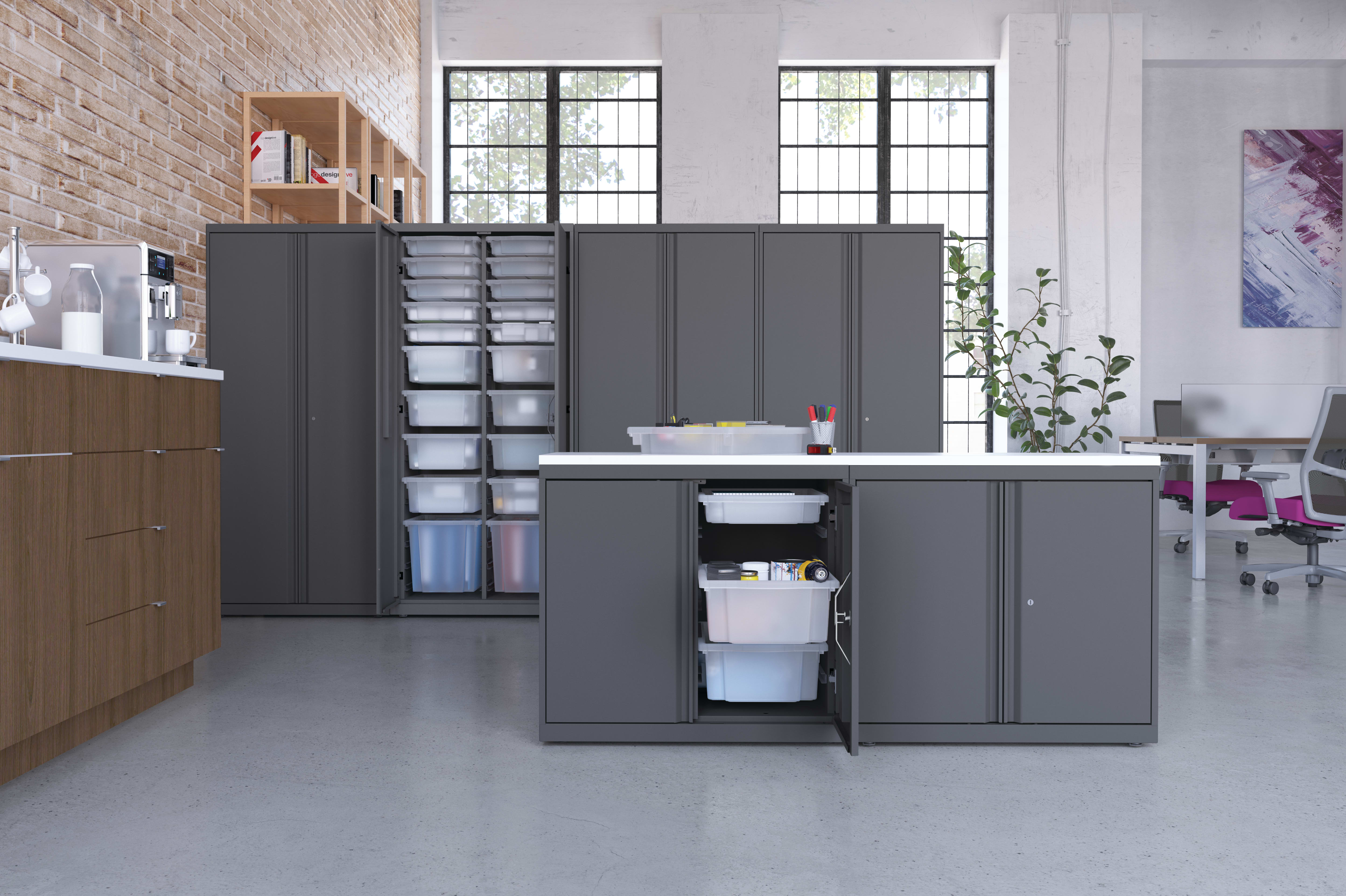 A modern, minimalist office space with gray storage cabinets, shelves, and drawers, complemented by large windows that let in natural light.