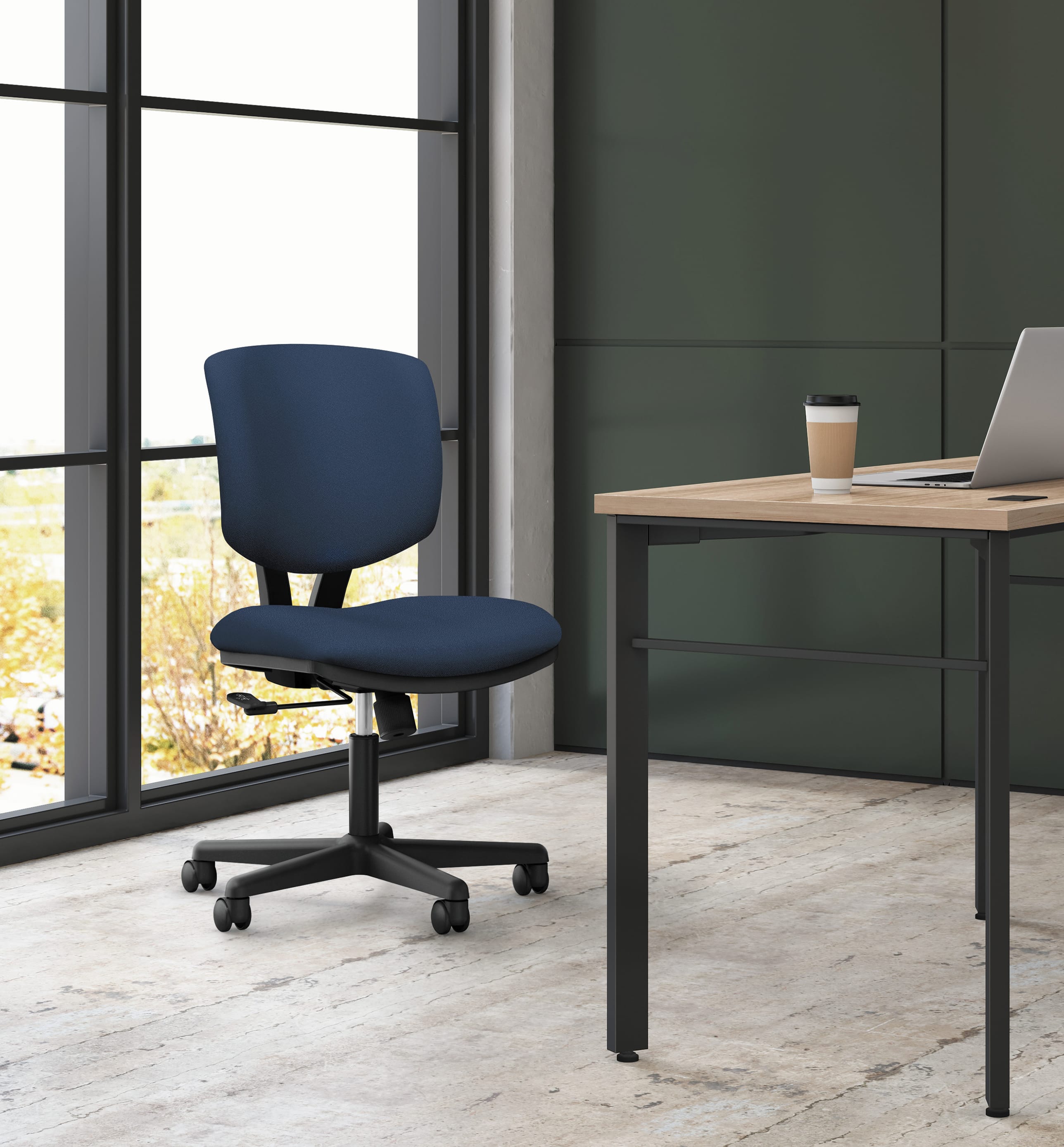 A modern office space with a navy blue office chair and a wooden desk with a laptop and a coffee cup placed on it, set against a large window overlooking a natural landscape.
