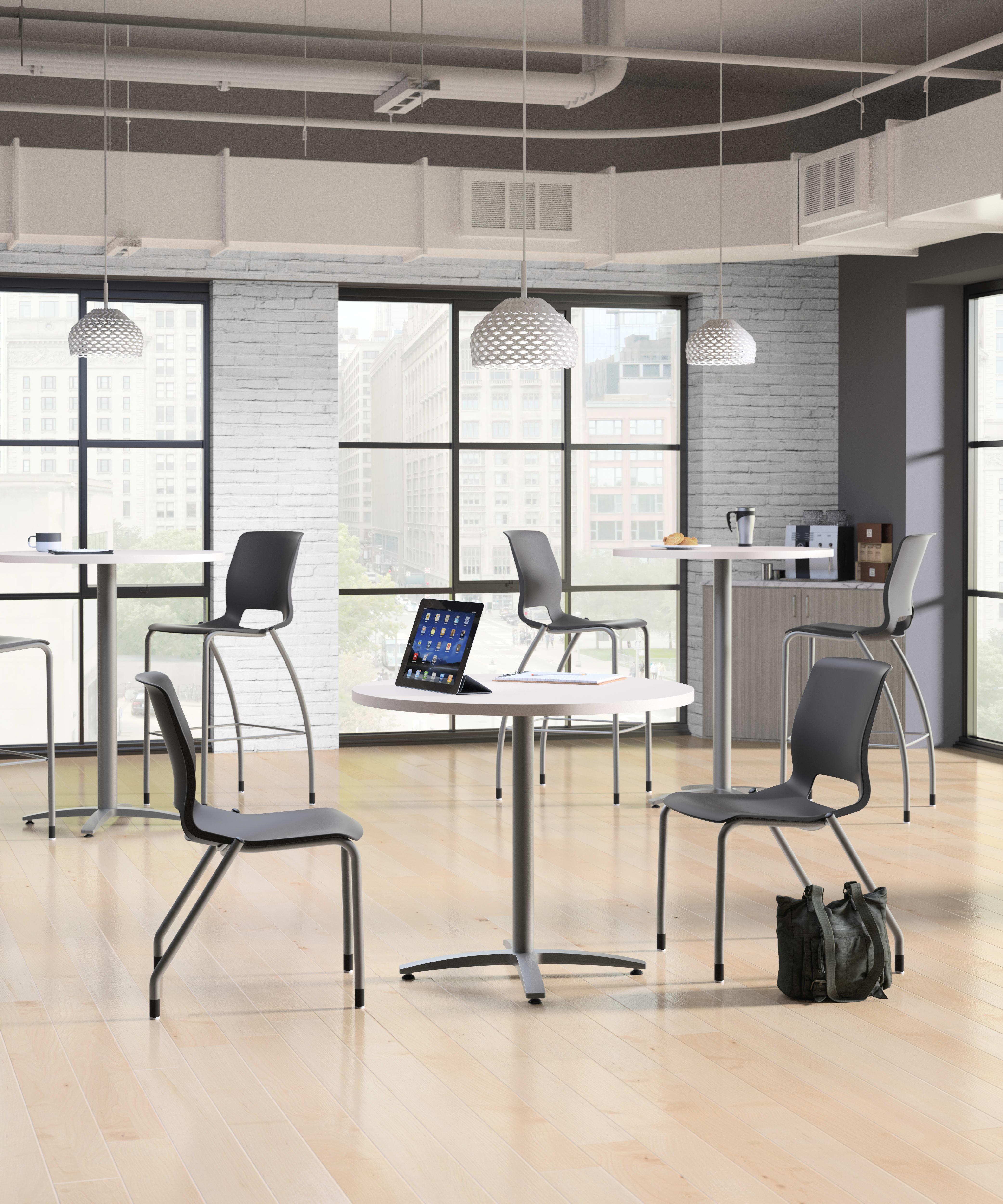 A modern, minimalist office space with desks, chairs, and a laptop on one of the tables, set against a backdrop of large windows and exposed brick walls.
