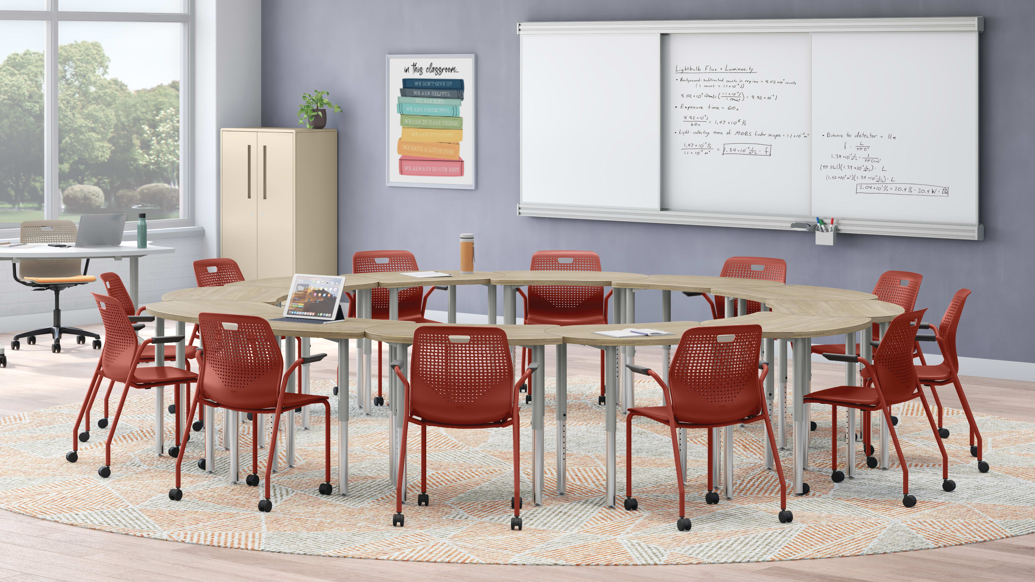 A modern, well-equipped classroom with a large oval table surrounded by red chairs, a whiteboard on the wall, and a storage cabinet in the background.