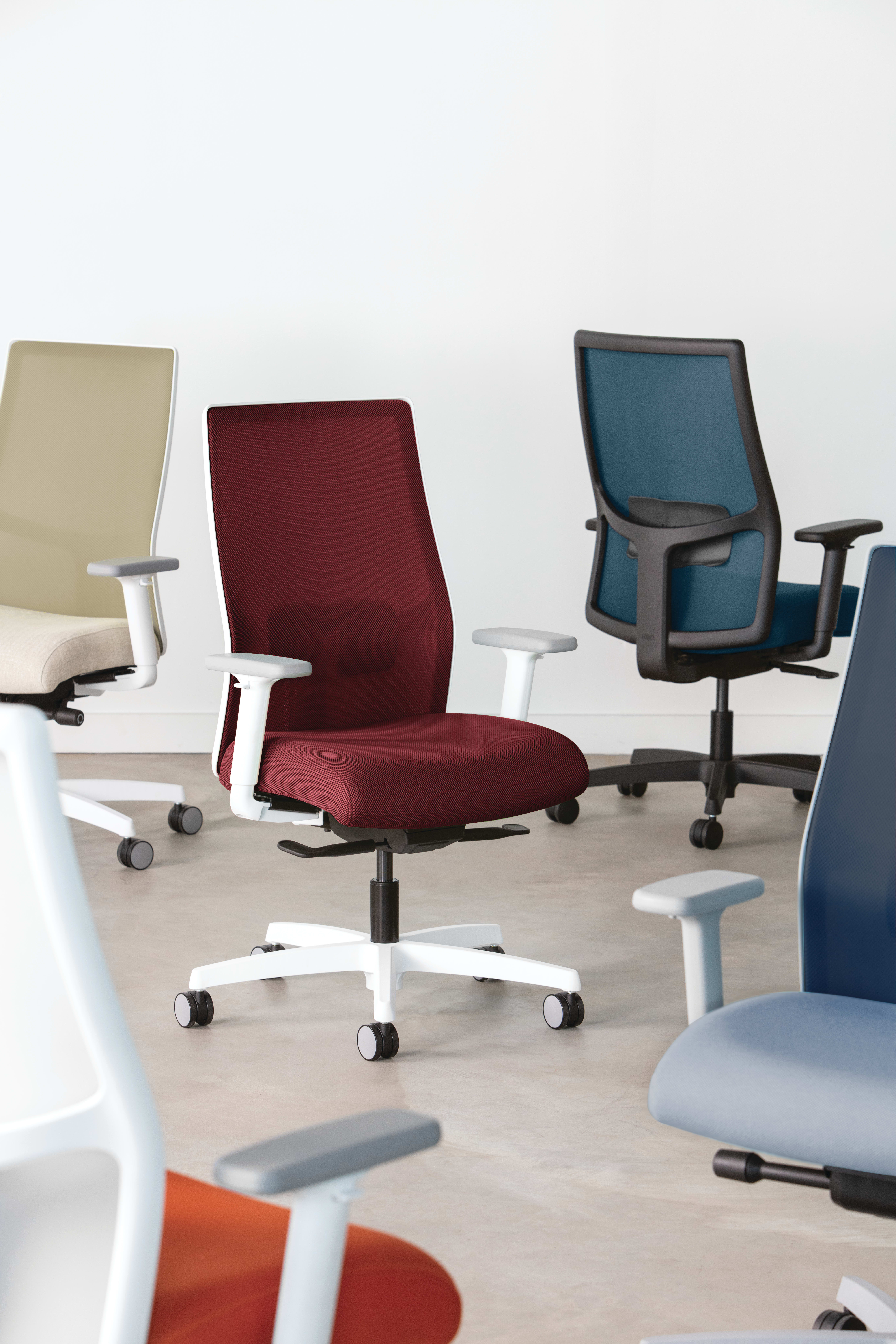 The image depicts a collection of modern office chairs in various colors, including beige, brown, and purple, arranged on a light-colored floor.