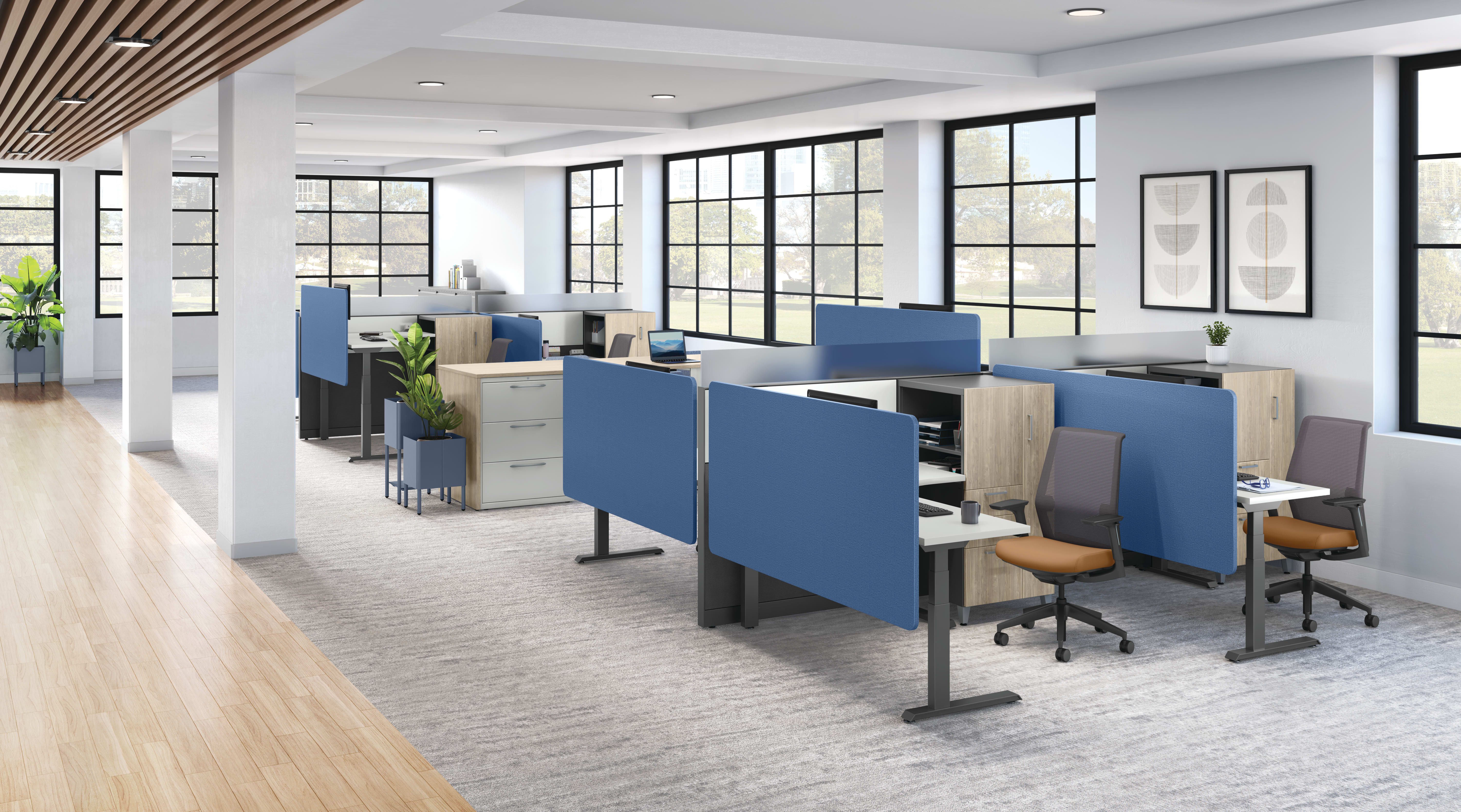 Modern open office layout with blue fabric cubicle panels, wood storage units, ergonomic task chairs, and large grid windows bringing in natural light.