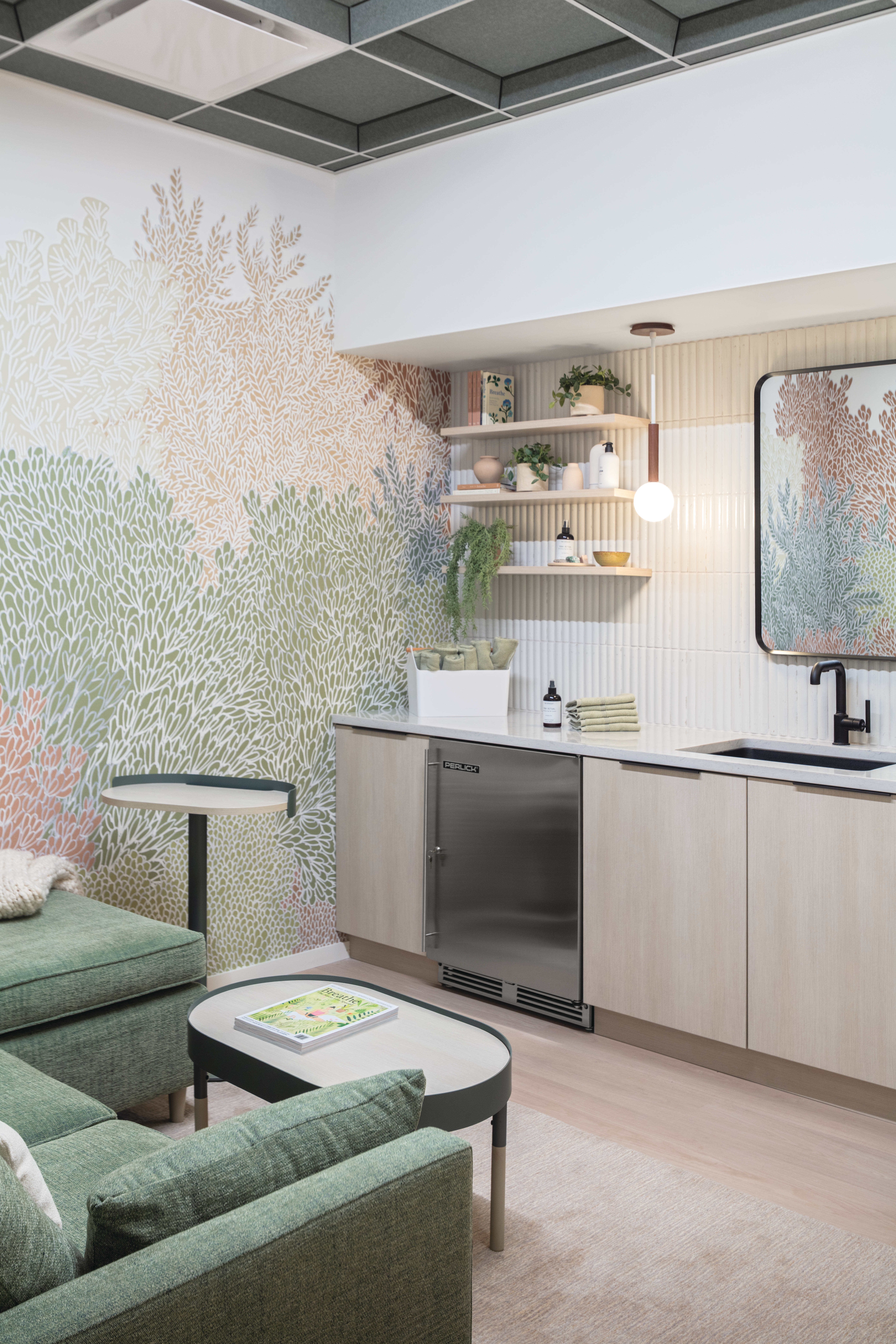 Lounge area with upholstered armchairs, soft seating, nested tables, side table, built-in cabinetry with integrated refrigeration, open shelving, pendant lighting, and decorative wall panels.