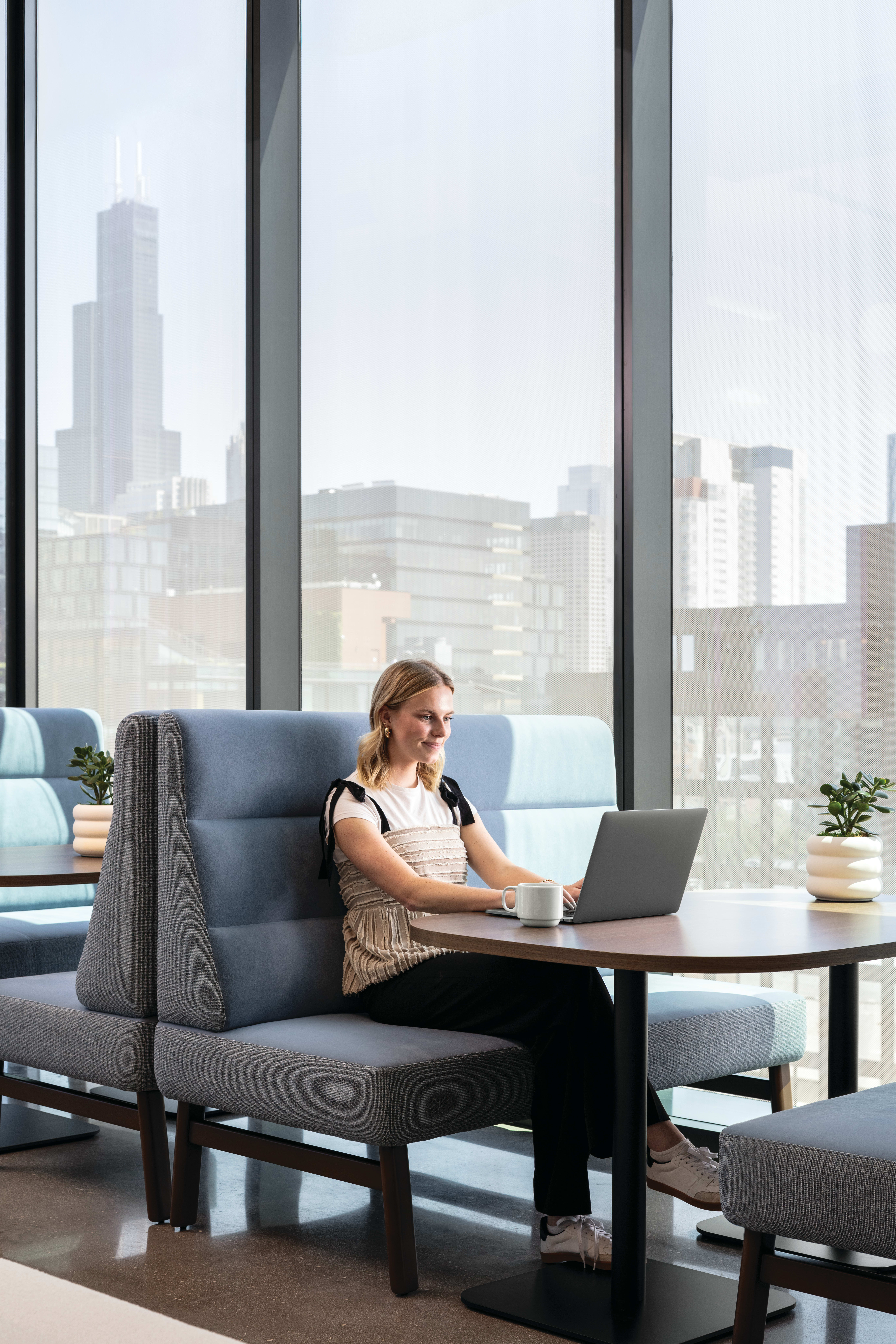 Round pedestal table with wood top and black base, paired with soft seating for casual work or conversation.