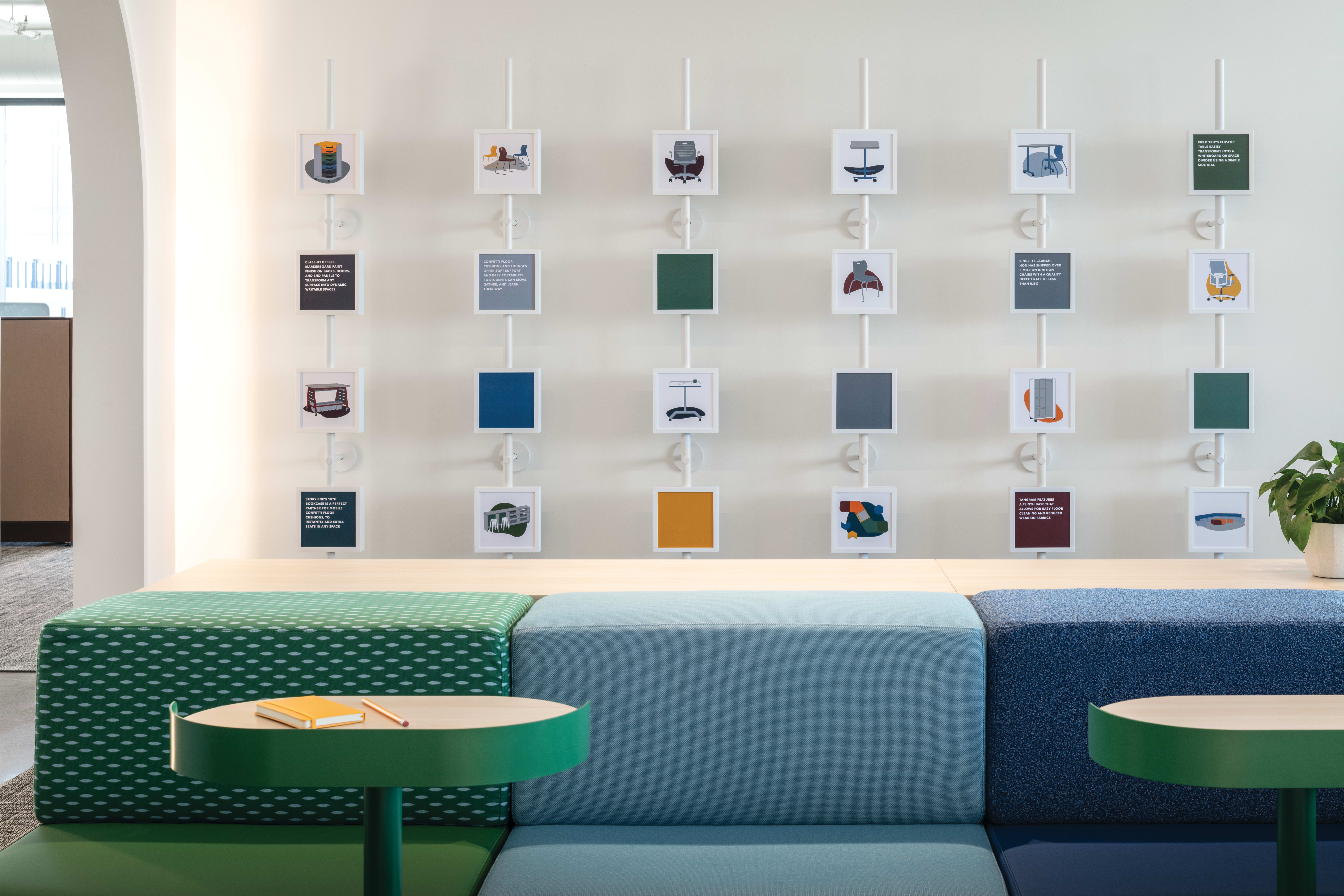 Modular upholstered bench seating with patterned and textured fabrics, round café tables in contrasting finishes, and coordinated display wall system with framed product visuals.