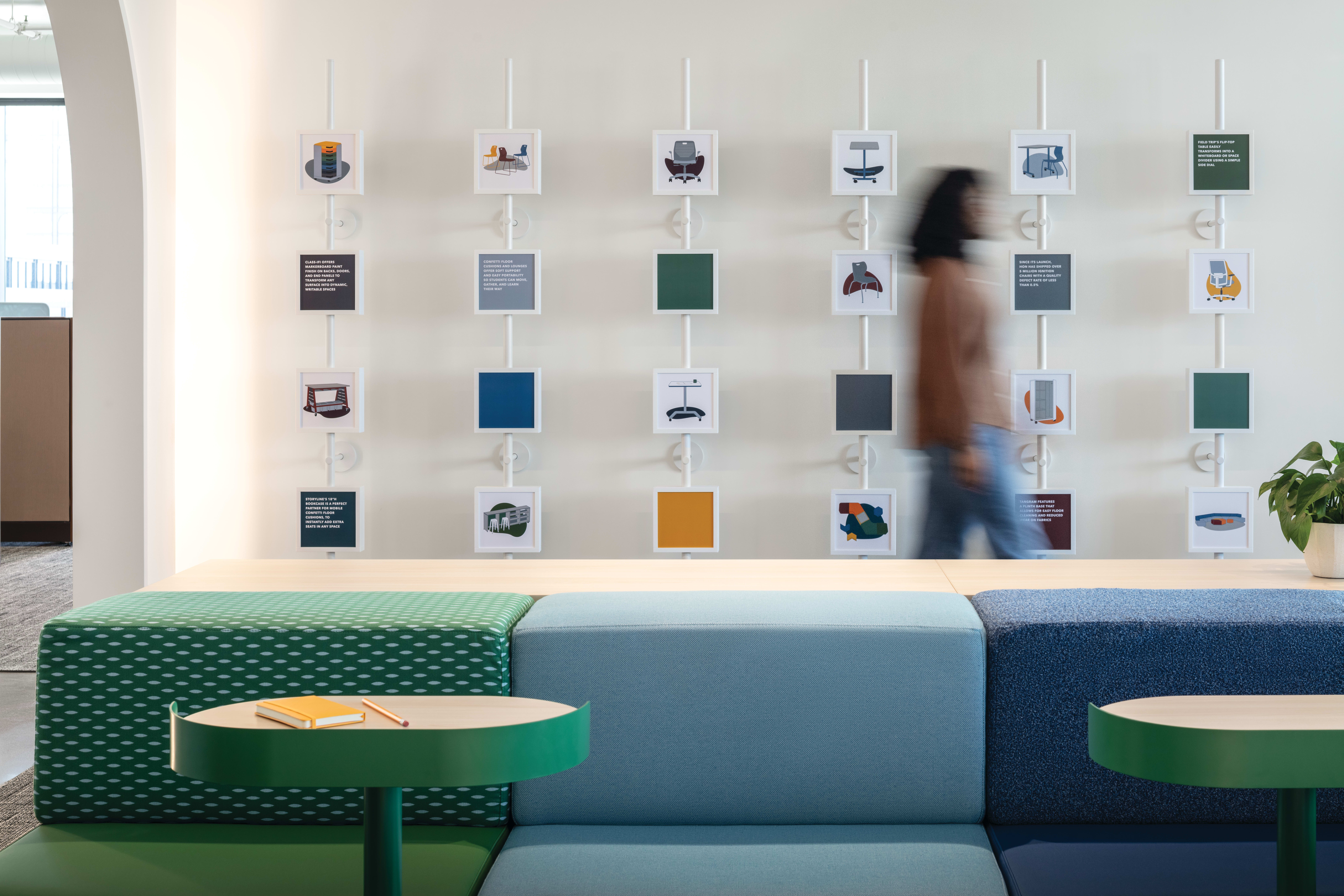 Modular upholstered bench seating with patterned and textured fabrics, round café tables in contrasting finishes, and coordinated display wall system with framed product visuals.