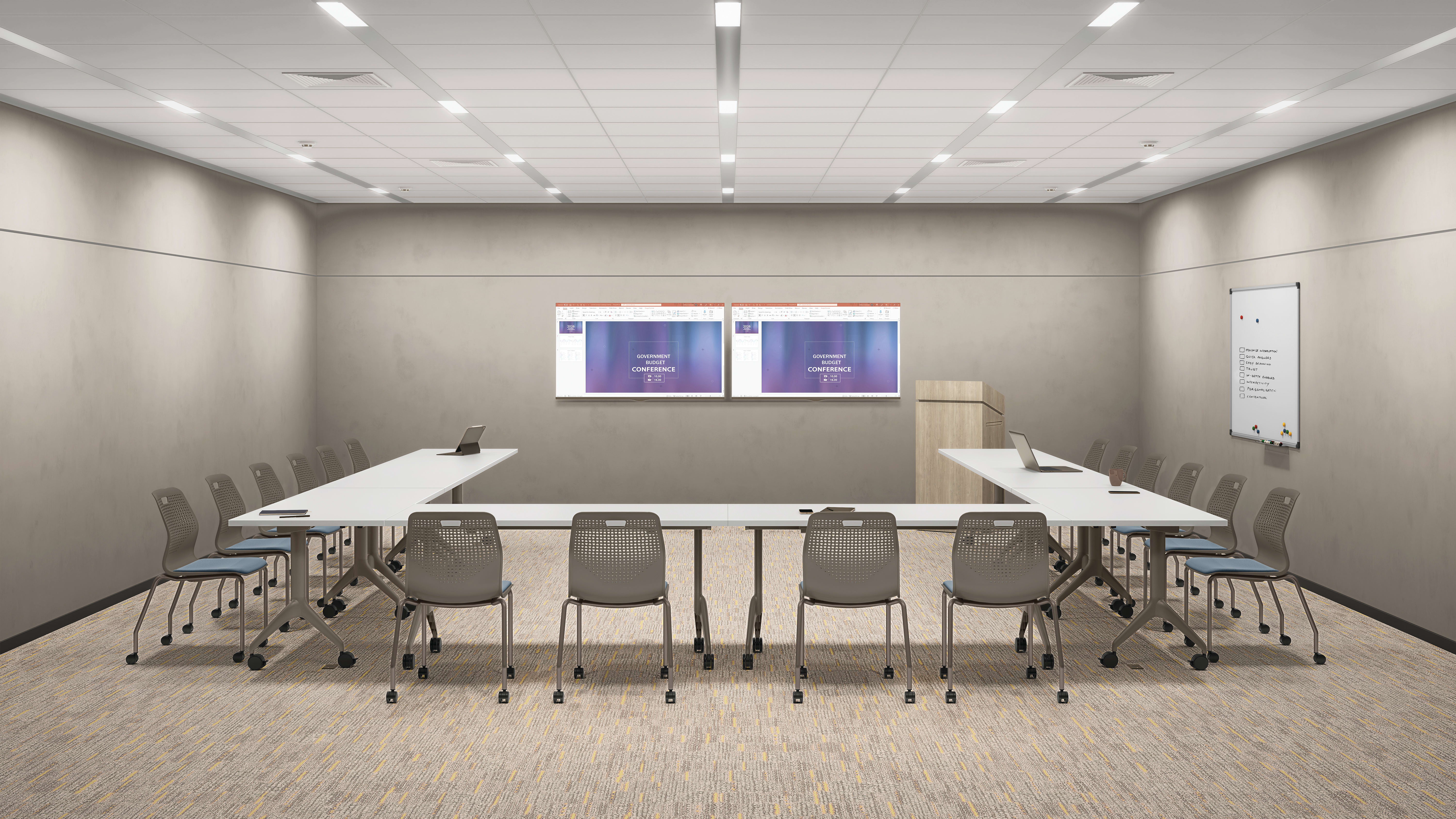 Modern training room with U-shaped tables, stackable chairs on casters, dual wall-mounted displays, lectern, whiteboard, and recessed ceiling lighting in a clean professional space.