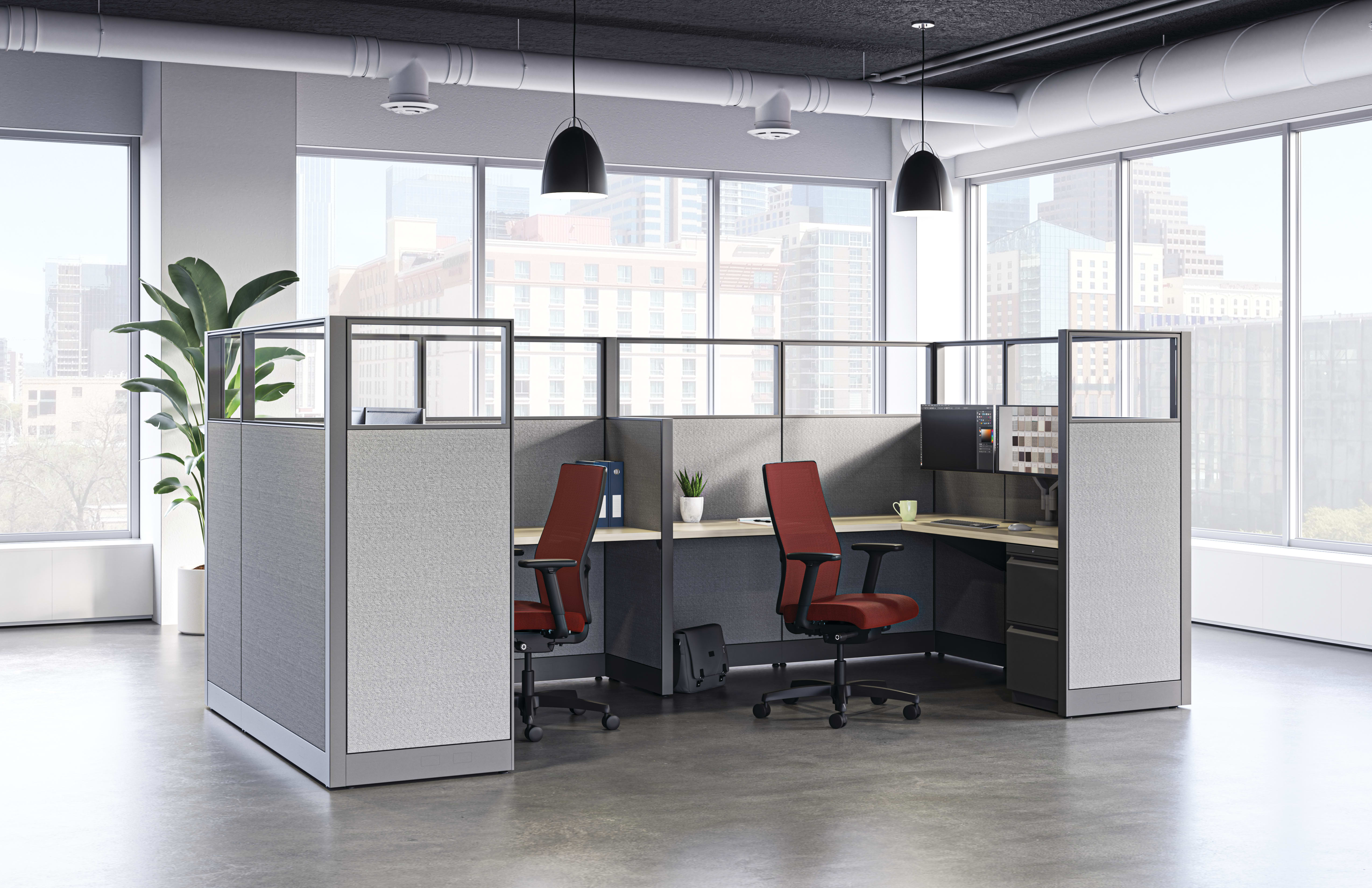 Modern open office with four gray-paneled workstations, red task chairs, and large windows showing a city skyline.