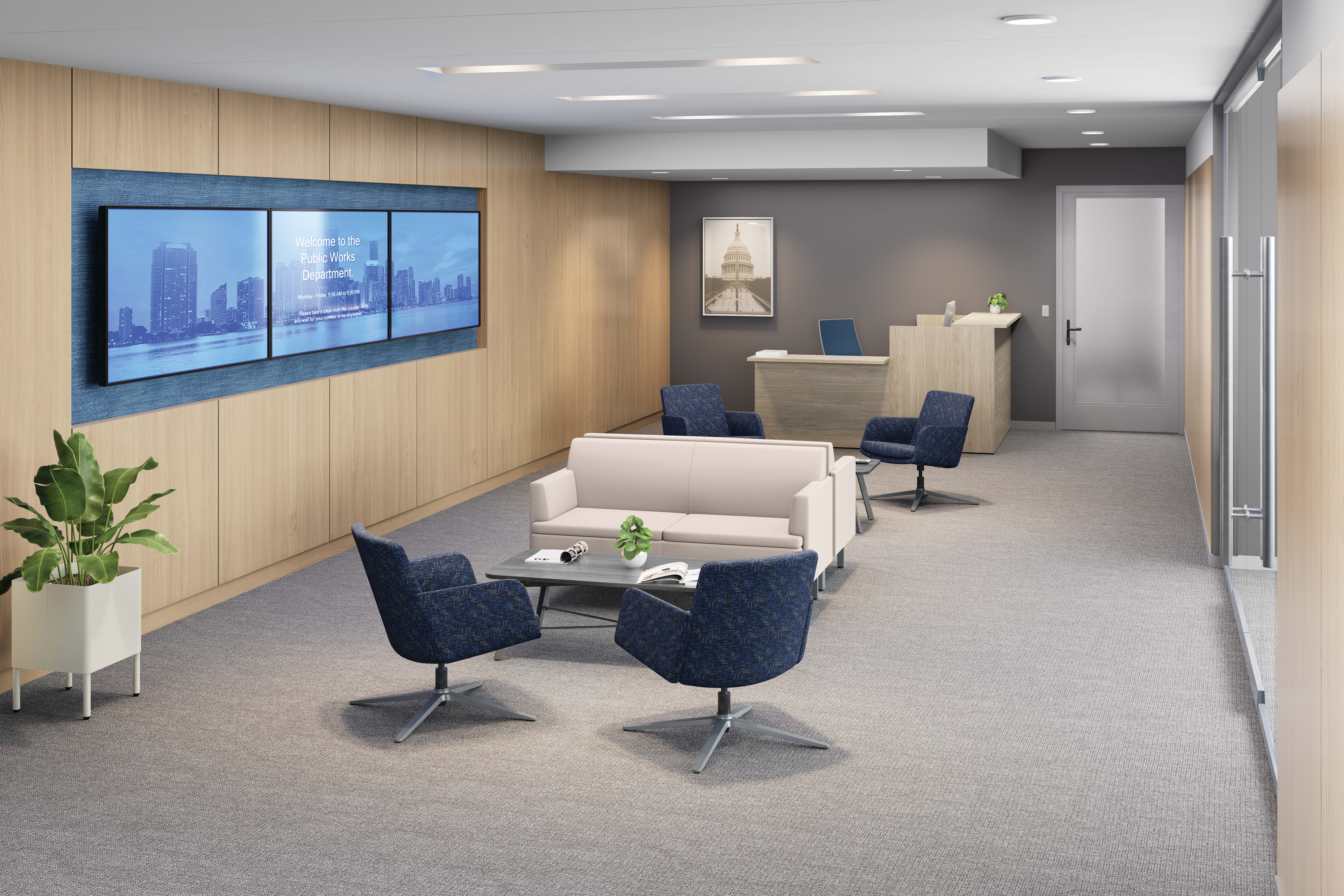 Modern office lounge with white sofa, blue lounge chairs, wall-mounted digital display, wood paneling, and reception desk.
